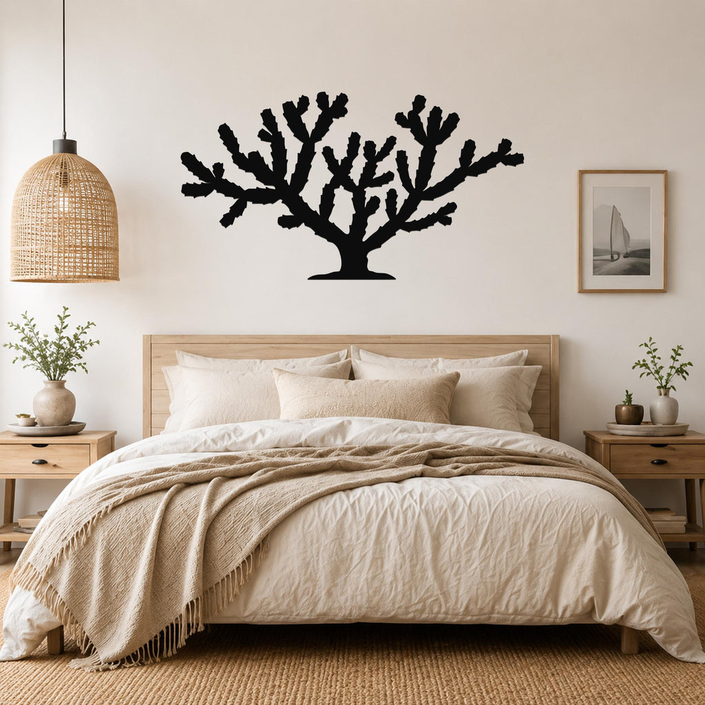 Black metal Cholla cactus wall art silhouette with branching arms, mounted above a bed in a neutral bedroom.