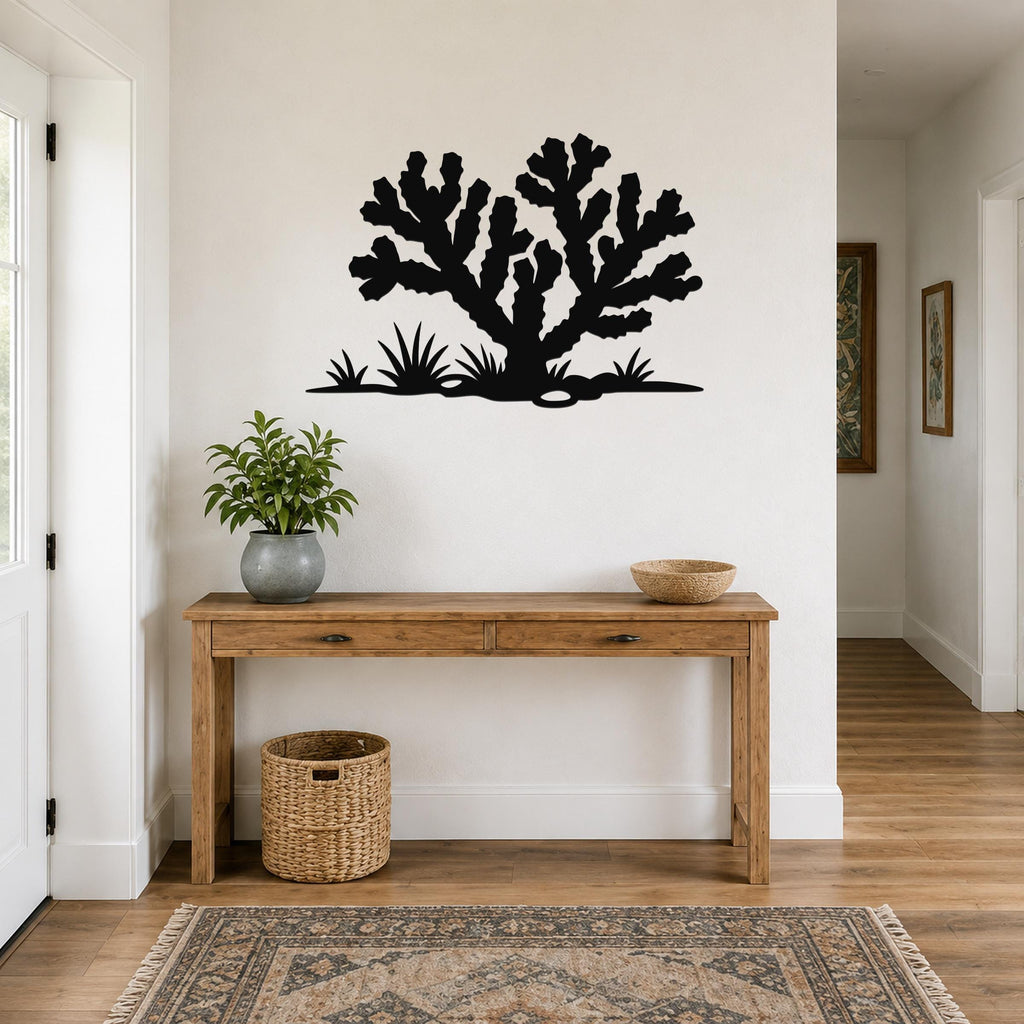 Black metal Cholla cactus wall art with branching silhouette and ground-level grass cutouts, mounted above a wooden console table in a bright entryway.