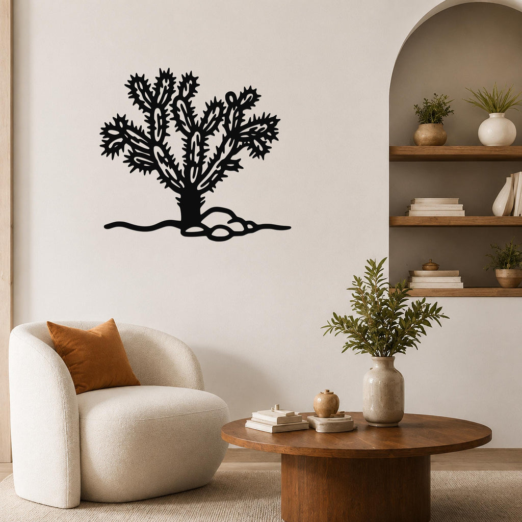 Black metal cholla cactus wall art with intricate branch cutouts, mounted on a living room wall above a white armchair.