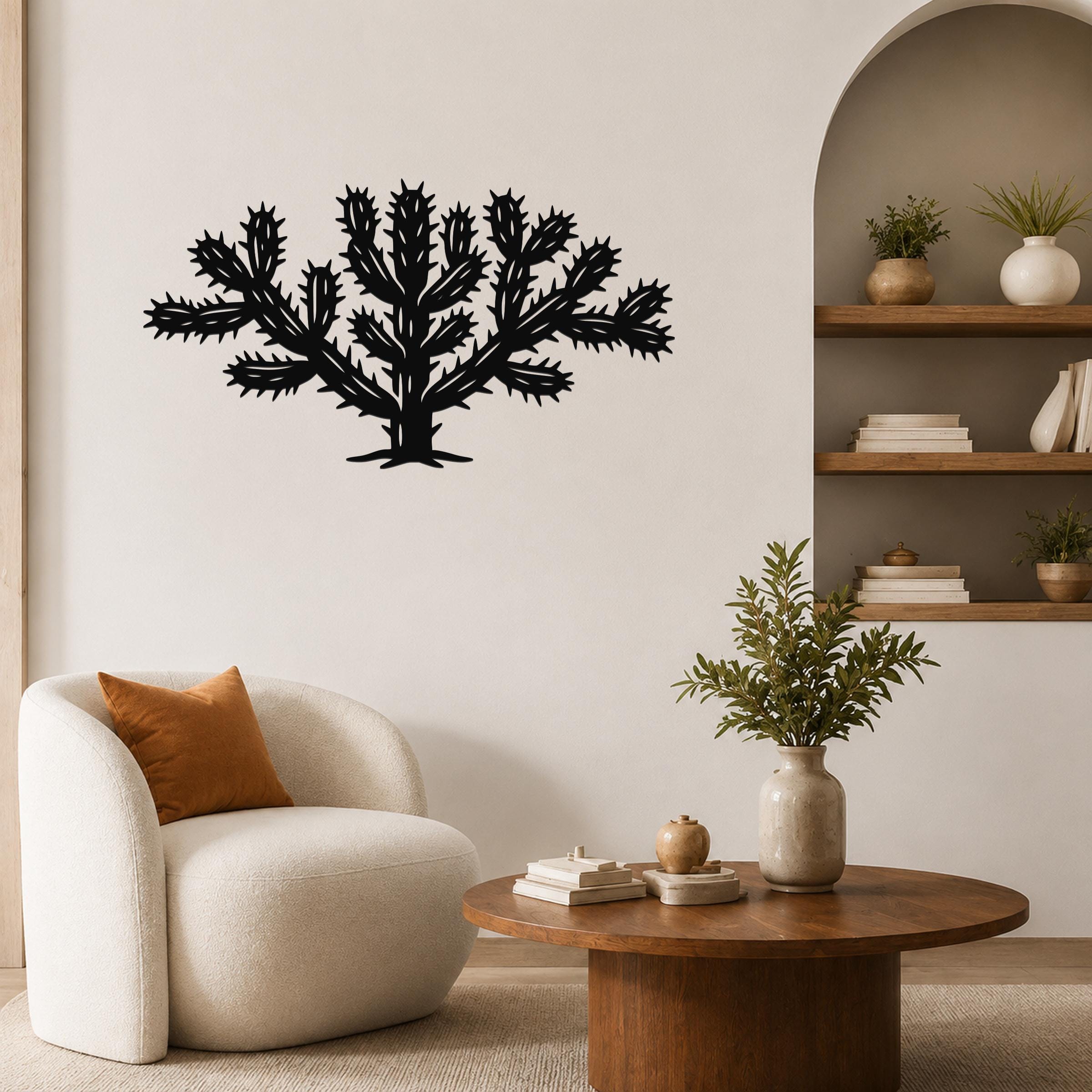 Black metal cholla cactus wall art with spiky branch cutouts, mounted on a living room wall above a white armchair.