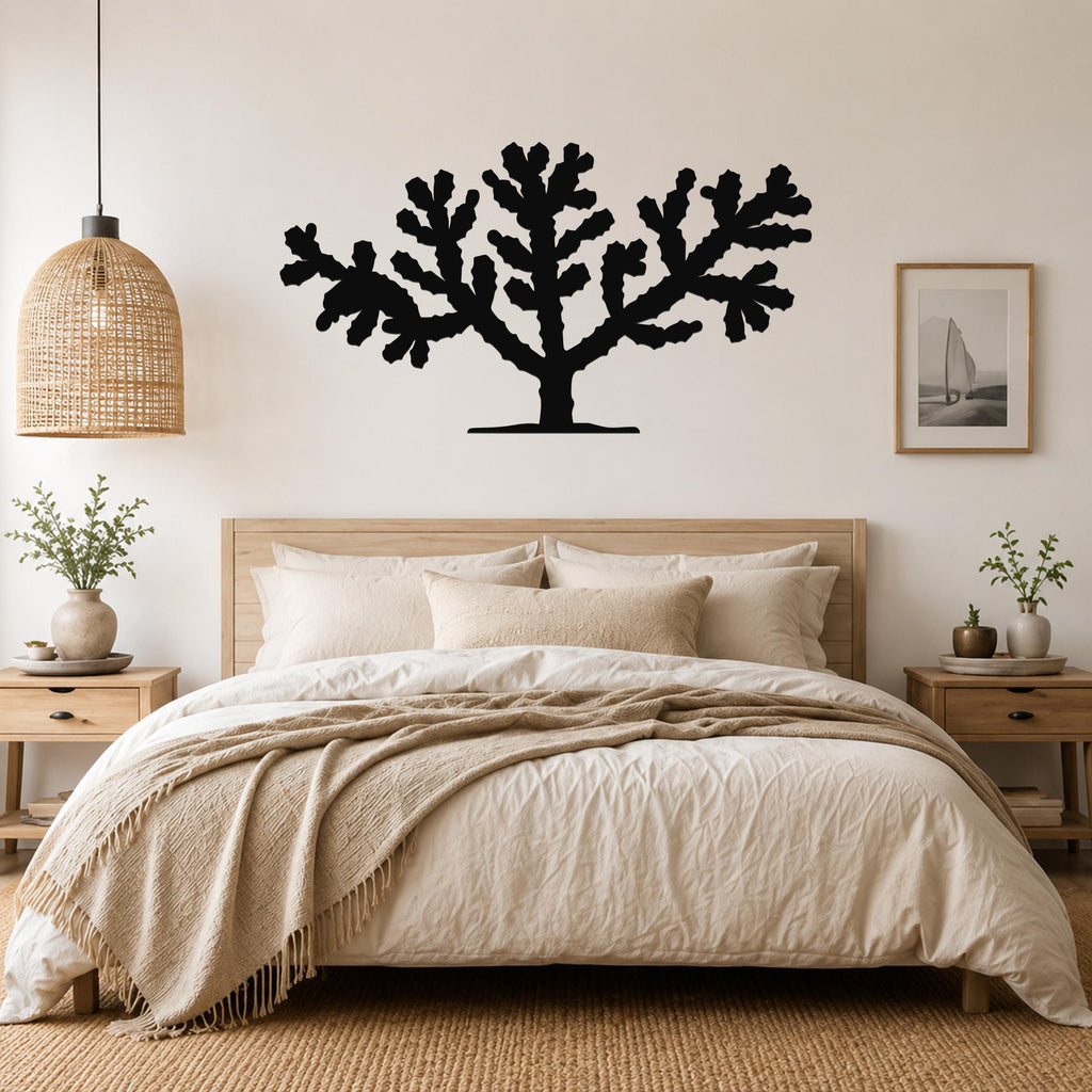 Black metal Cholla cactus wall art silhouette with branching arms, mounted above a wooden bed in a neutral bedroom.