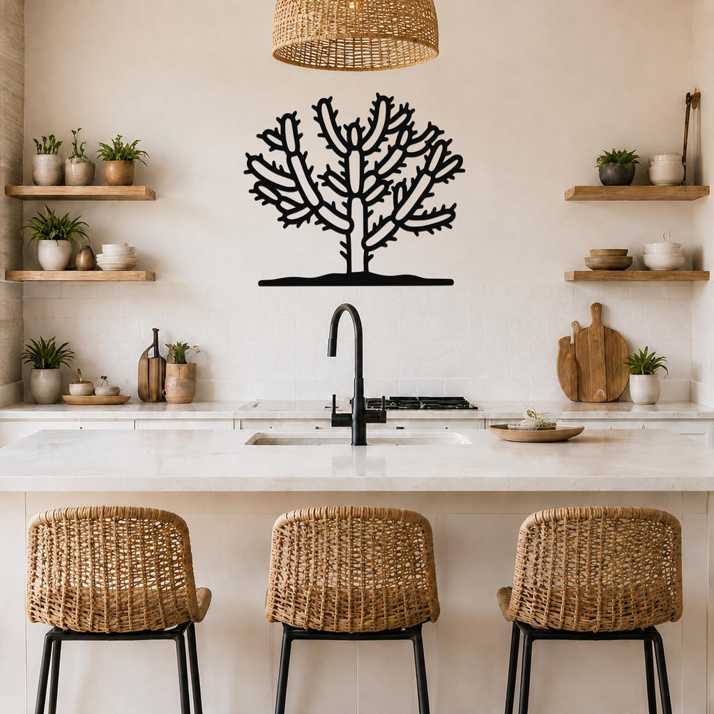Black metal Cholla cactus wall art with branching silhouette cutouts, mounted above a kitchen counter with a sink and wicker bar stools.