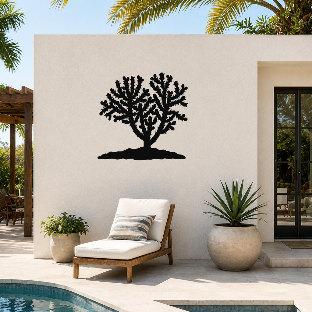 Black metal Cholla cactus wall art with branching cutouts, mounted on a white outdoor wall above a lounge chair near a pool.