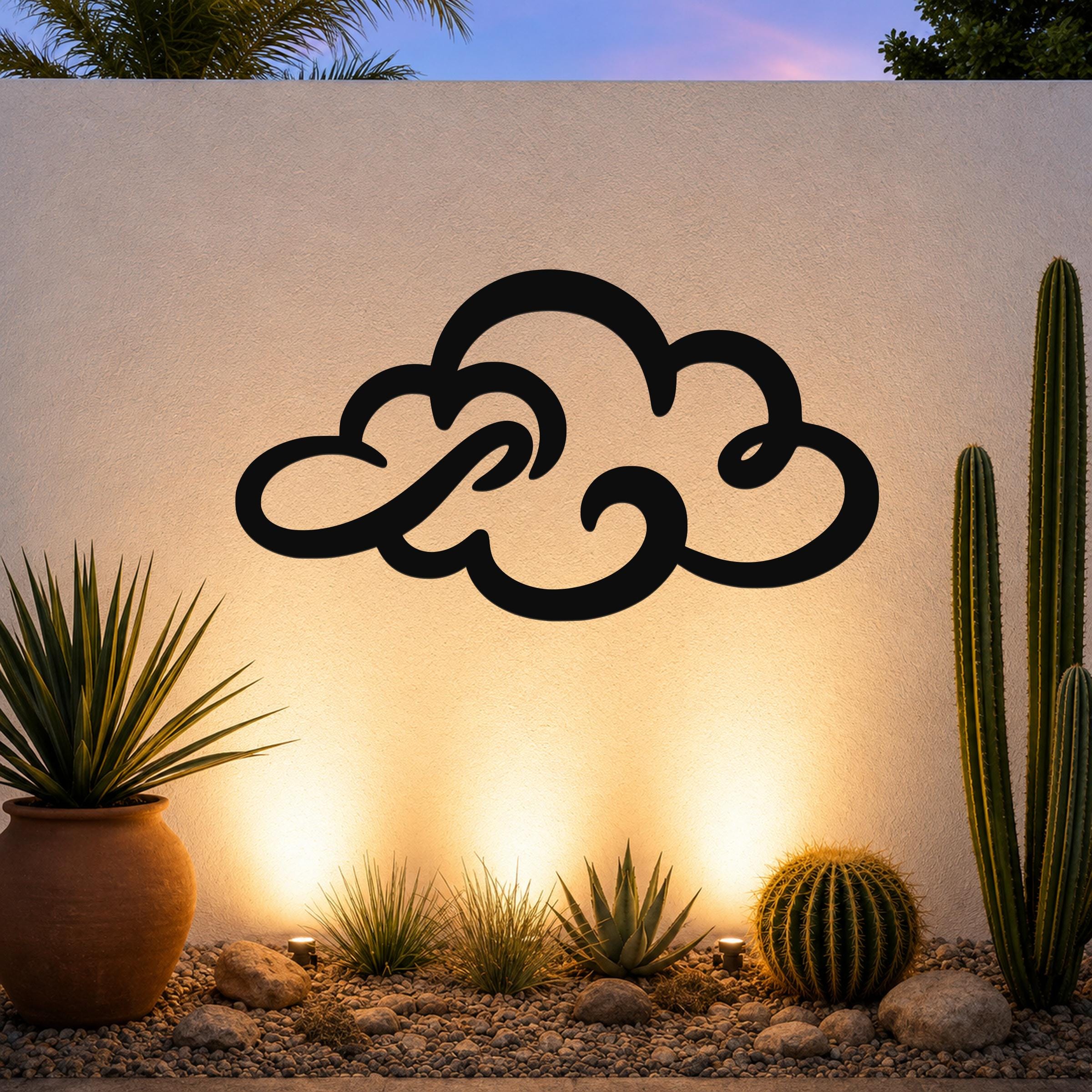 Black metal cloud wall art with flowing silhouette cutouts, mounted on an outdoor wall above a desert garden with cacti and warm ground lighting.