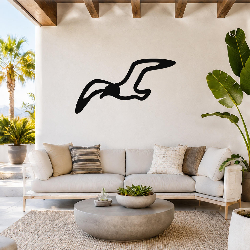 Black metal seagull wall art with a flowing silhouette, mounted above a white sofa in a bright living room.