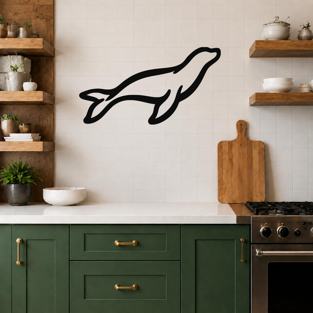 Black metal sea lion wall art silhouette mounted on a tiled kitchen wall above a counter, with wooden shelves and green cabinets visible.