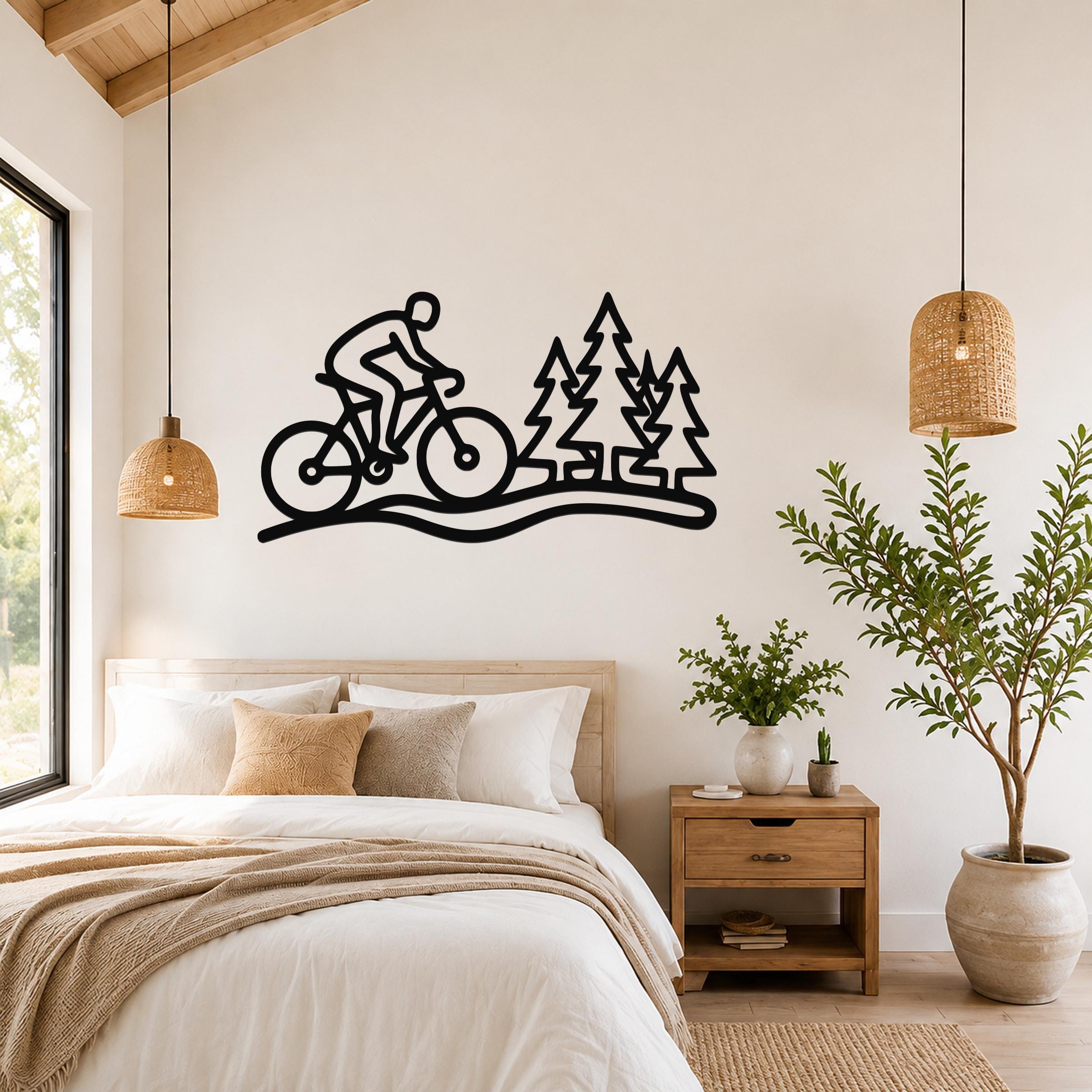 Black metal wall art silhouette of a cyclist on a trail with pine trees, mounted above a bed in a bedroom.