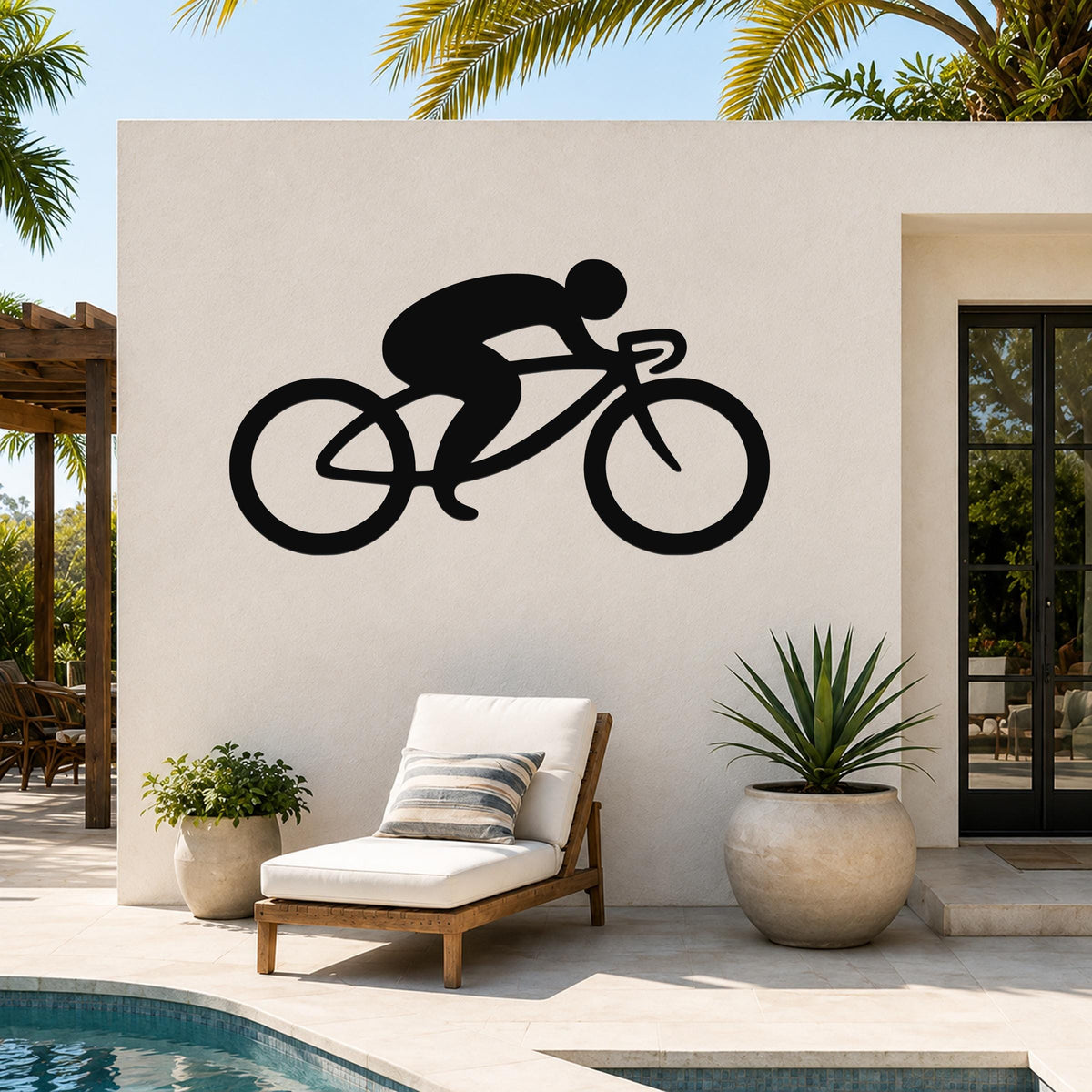Black metal cycling wall art silhouette of a rider on a road bike, mounted on an outdoor patio wall above a lounge chair and pool.