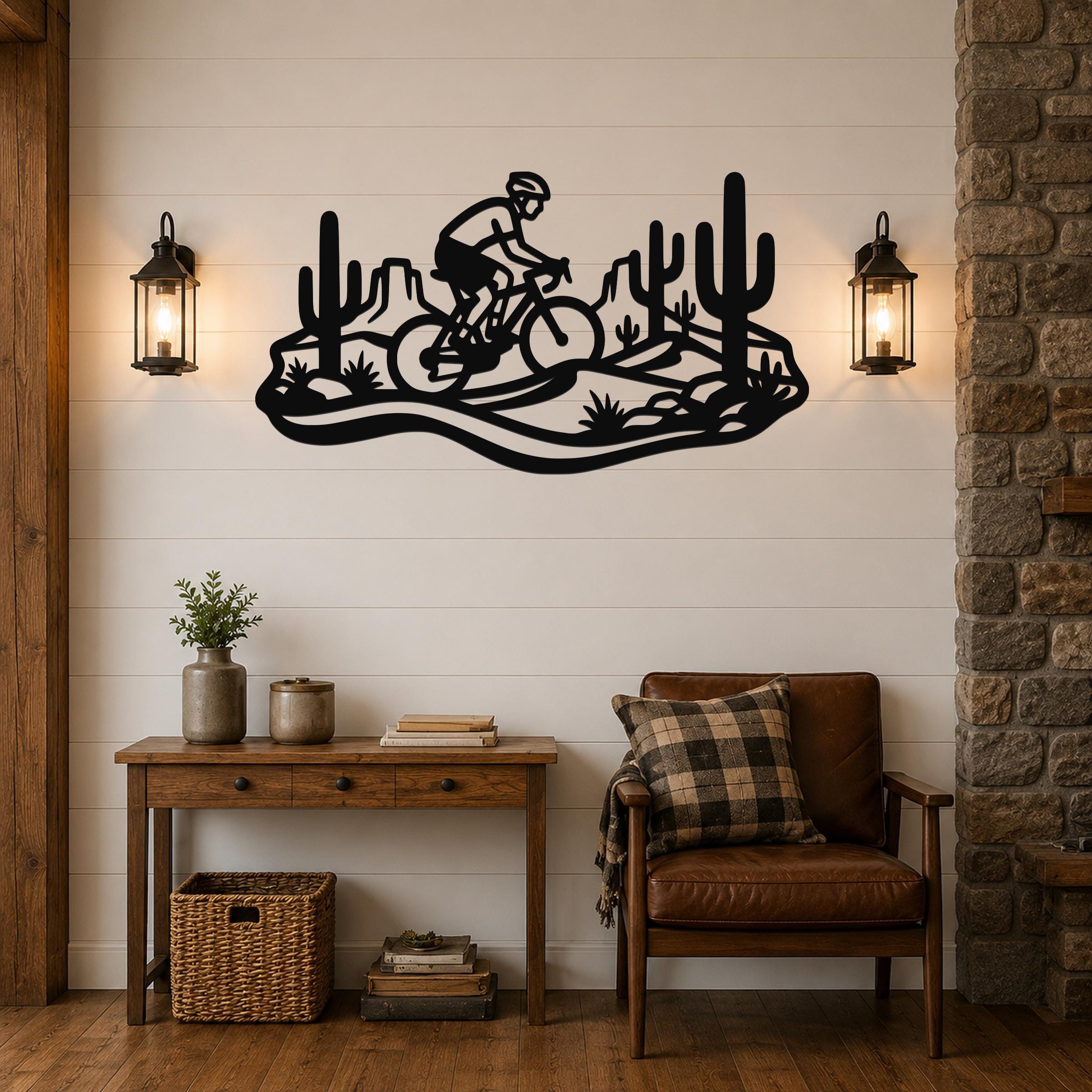 Black metal wall art featuring a mountain biker silhouette in a Sonoran Desert scene with cacti and rock formations, mounted on a shiplap wall above a wooden console table.