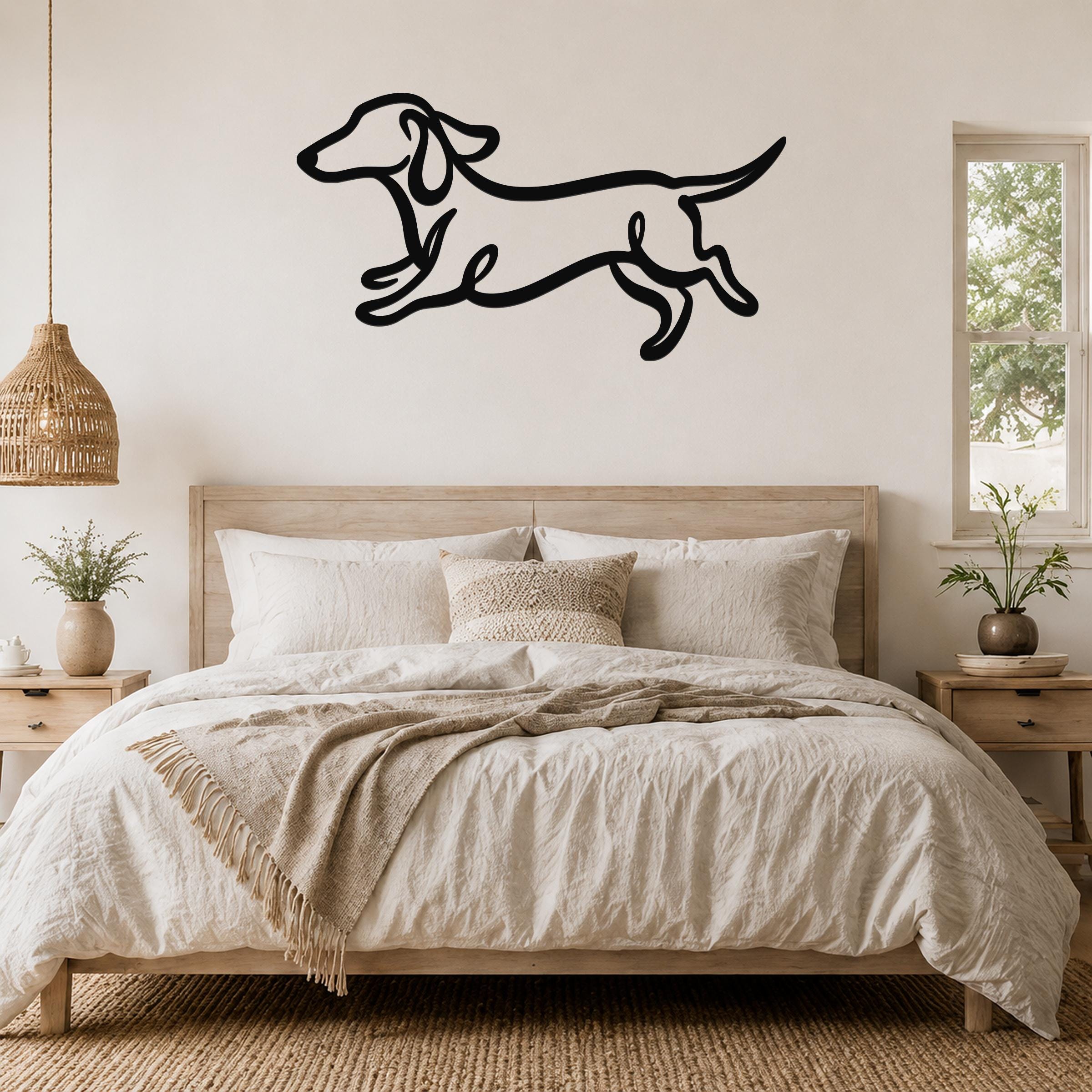 Black metal dachshund wall art with bold line cutout design, mounted above a wooden bed in a neutral bedroom.