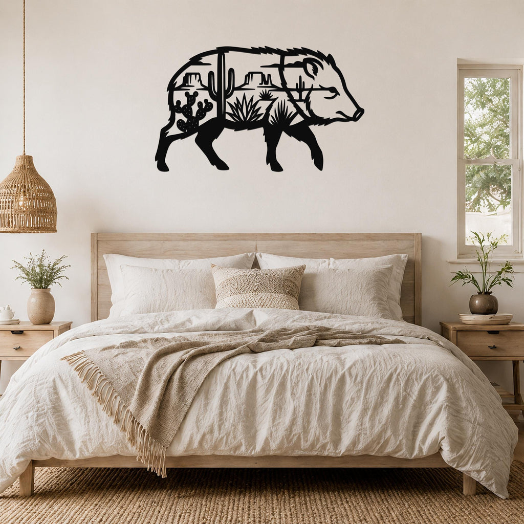 Black metal wall art of a javelina silhouette with desert landscape cutouts, mounted above a bed in a bedroom.
