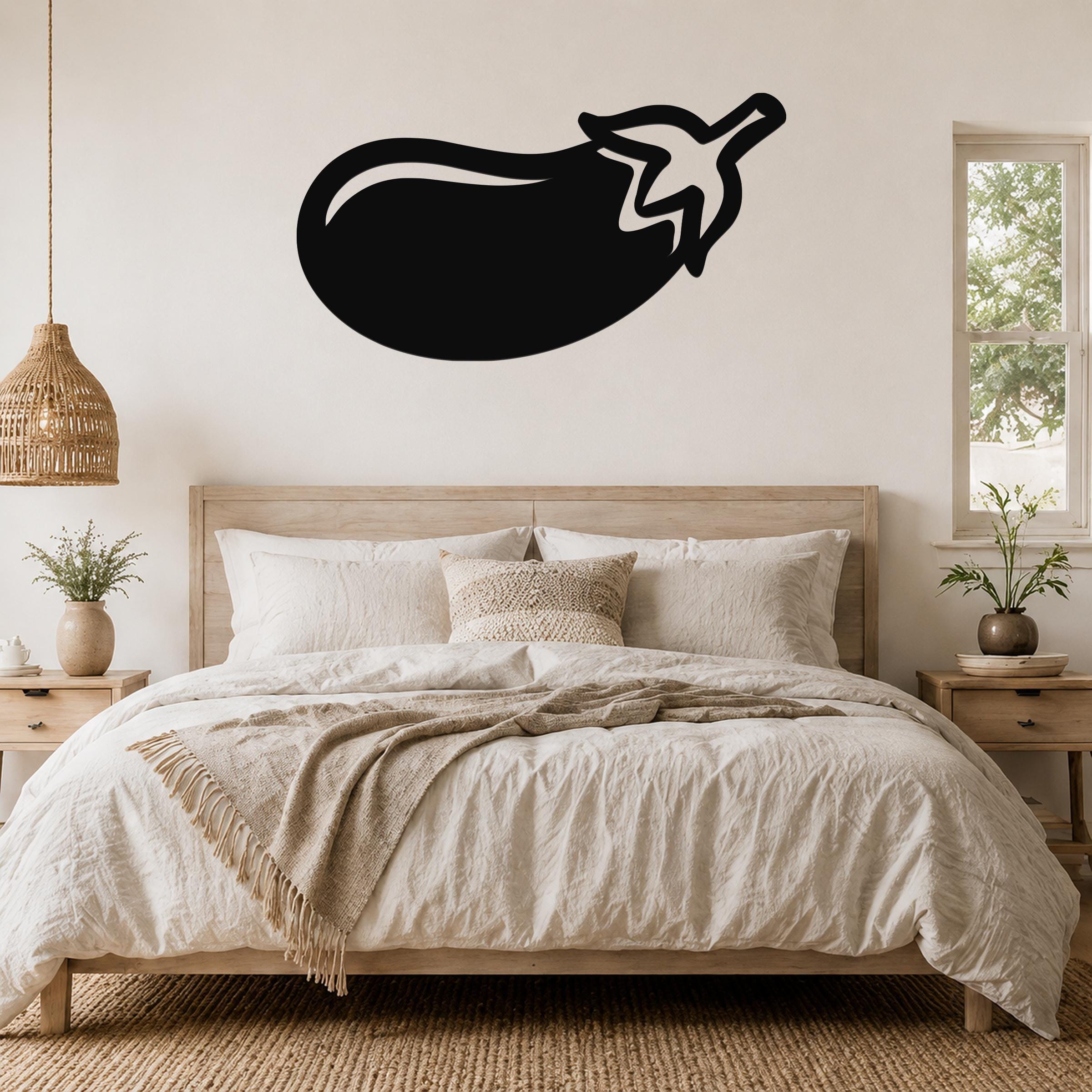 Black metal eggplant wall art with a white stem cutout, mounted above a wooden bed in a neutral bedroom.