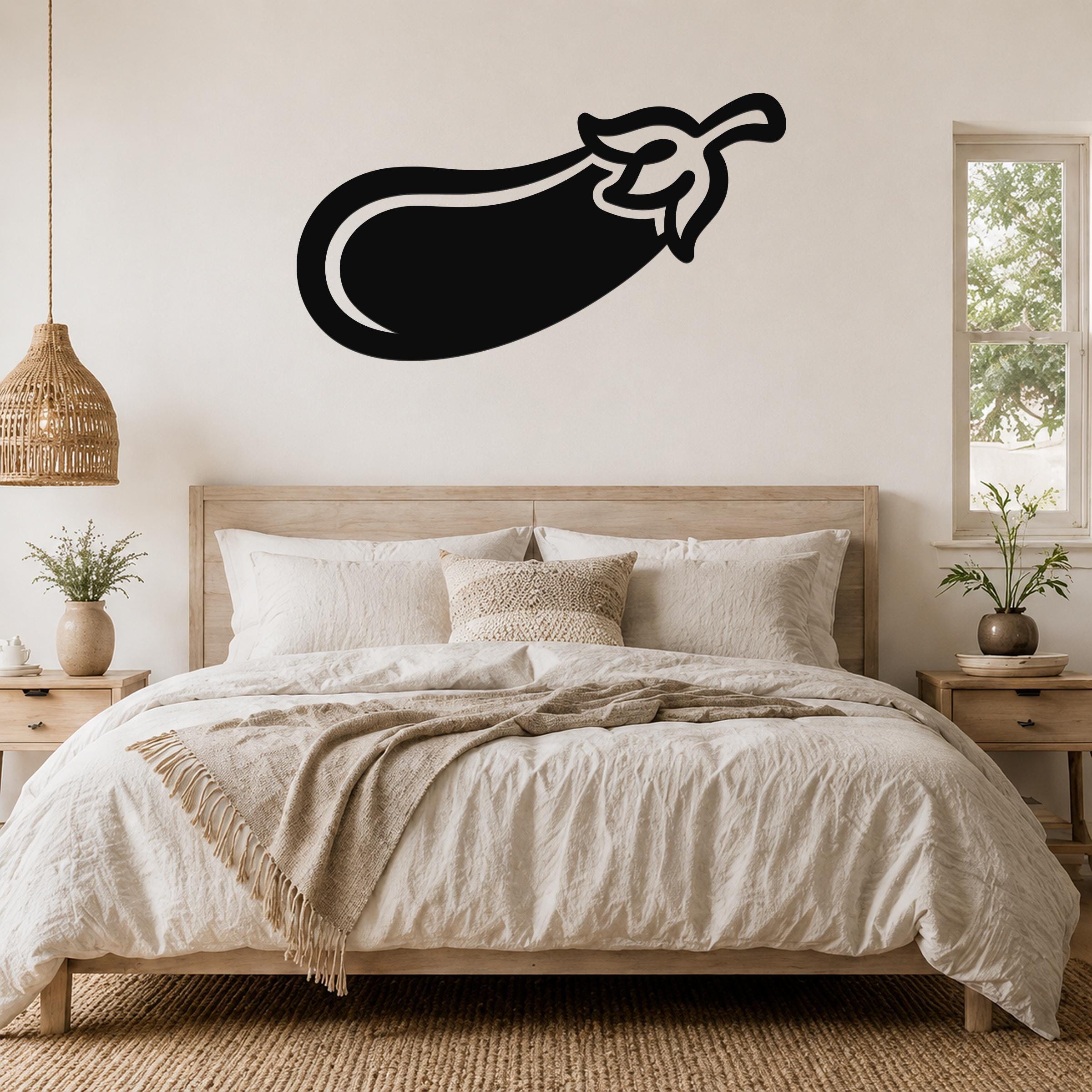 Black metal eggplant wall art with a leaf cutout, mounted above a bed in a neutral bedroom.