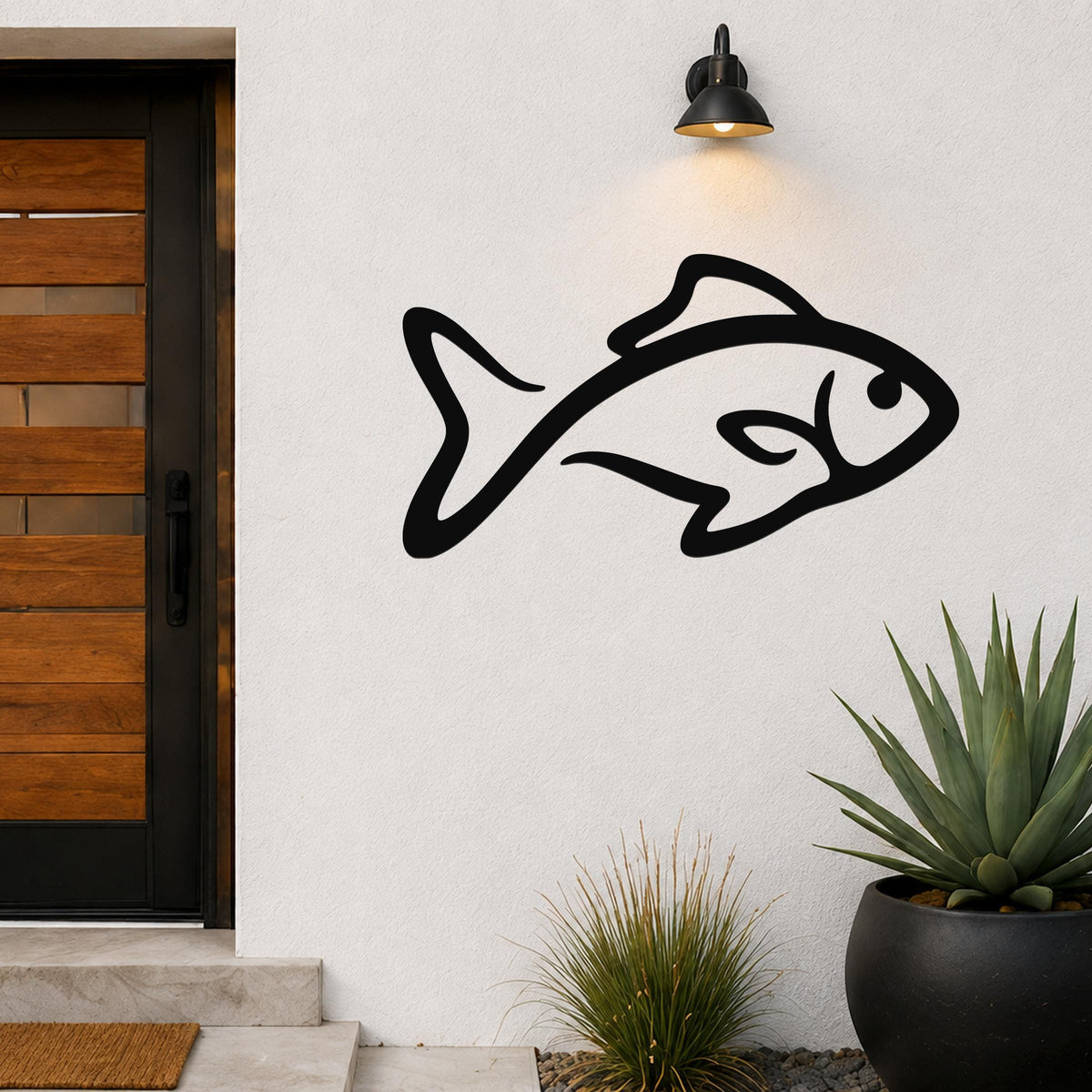Black metal fish silhouette wall art with internal cutout details, mounted on an outdoor wall beside a wooden door and potted plants.