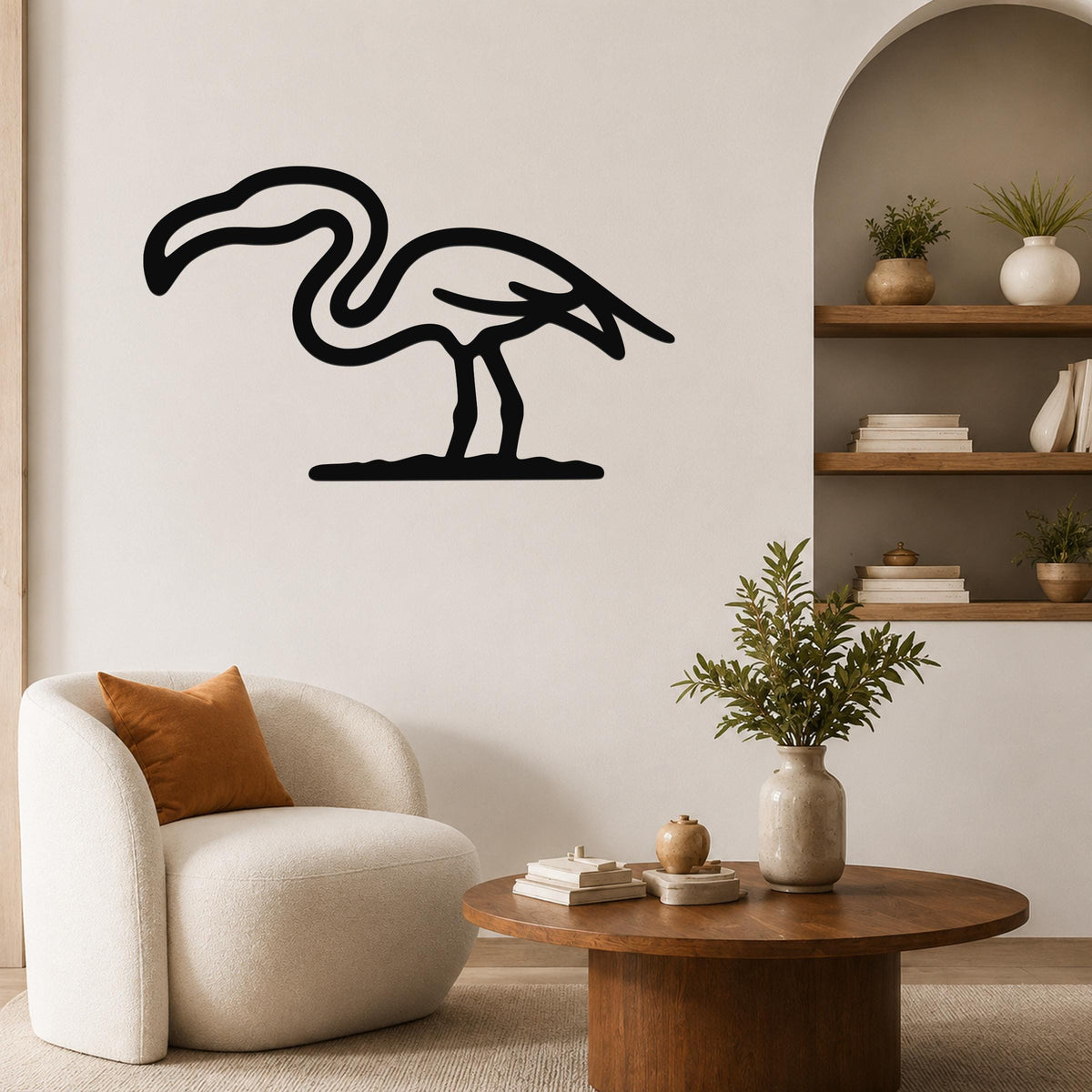 Black metal flamingo wall art silhouette mounted on a living room wall above a white armchair.