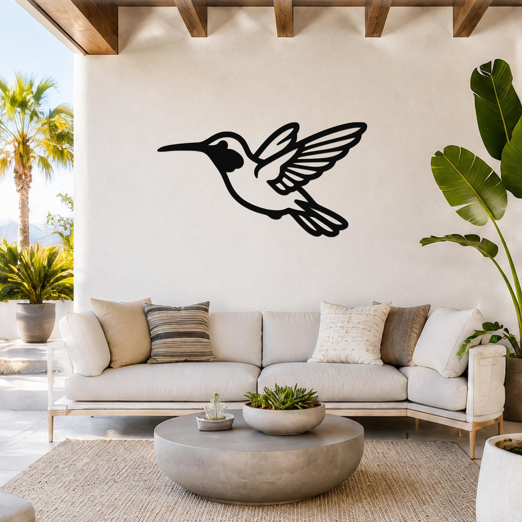 Black metal hummingbird wall art with wing and tail cutouts, mounted above a white sofa in a bright living room.