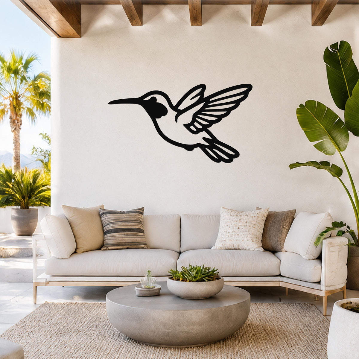 Black metal hummingbird wall art with wing and tail cutouts, mounted above a white sofa in a bright living room.