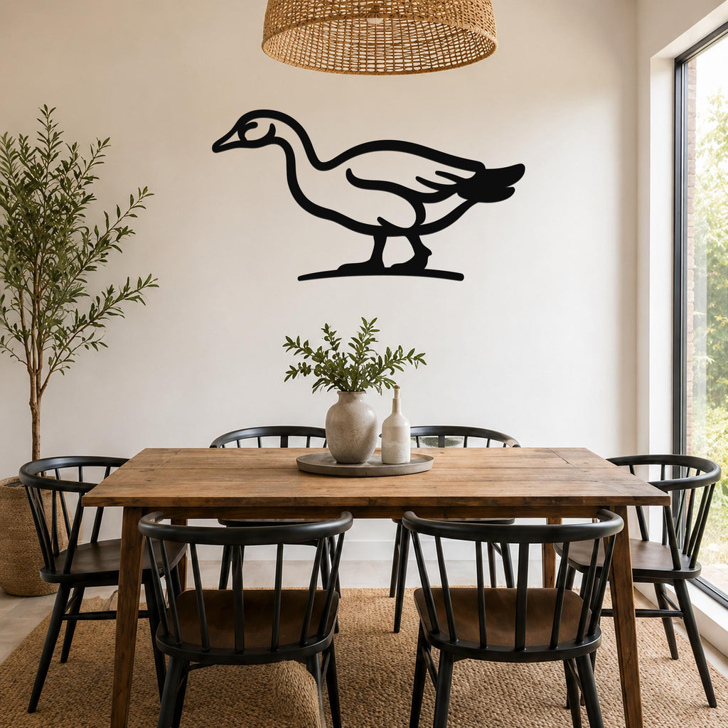 Black metal goose wall art silhouette mounted on a white wall above a wooden dining table in a bright dining room.