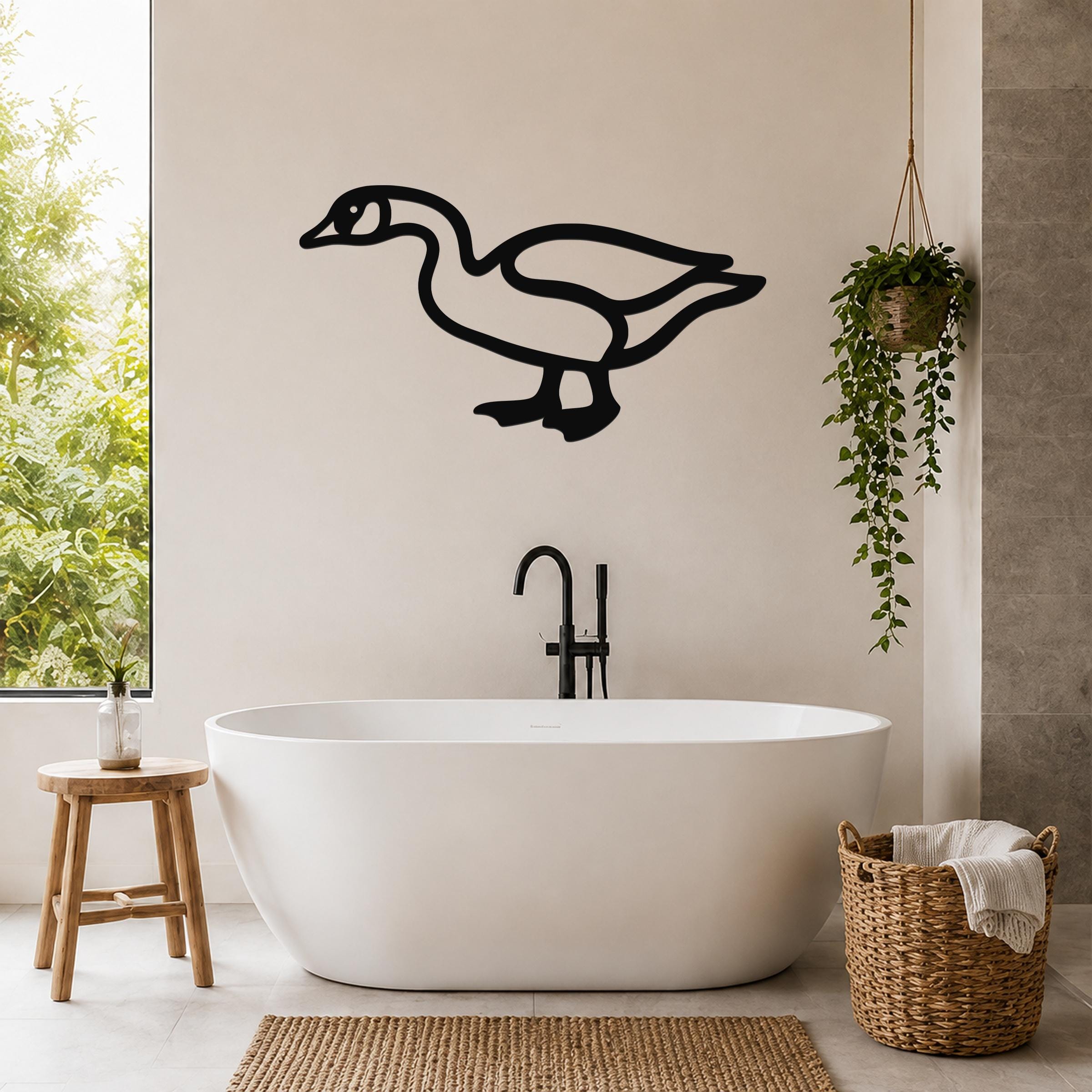 Black metal goose wall art silhouette mounted on a bathroom wall above a freestanding tub, with a hanging plant and woven basket nearby.