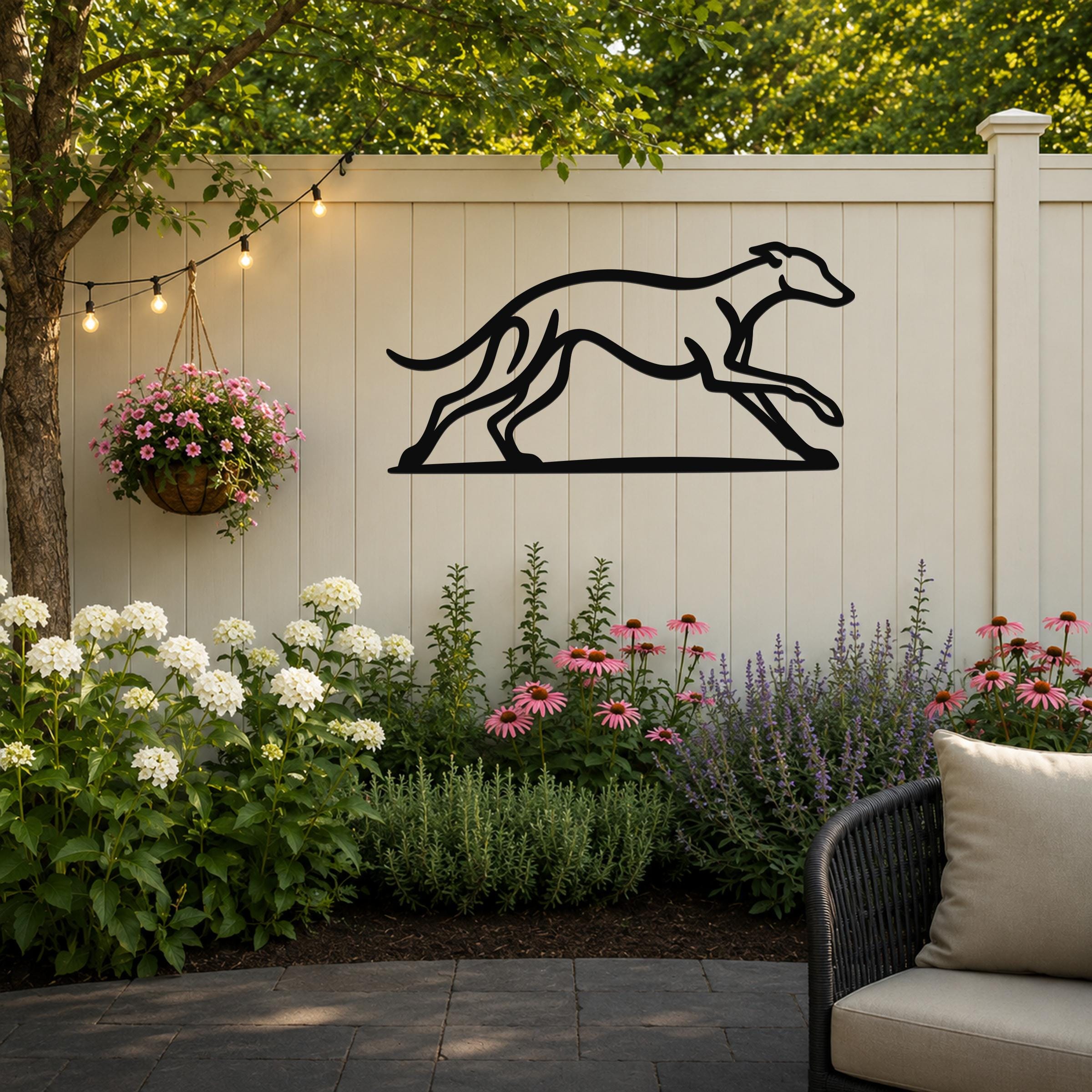 Black metal greyhound wall art with a minimalist silhouette design, mounted on a light-colored outdoor fence above a flower bed.