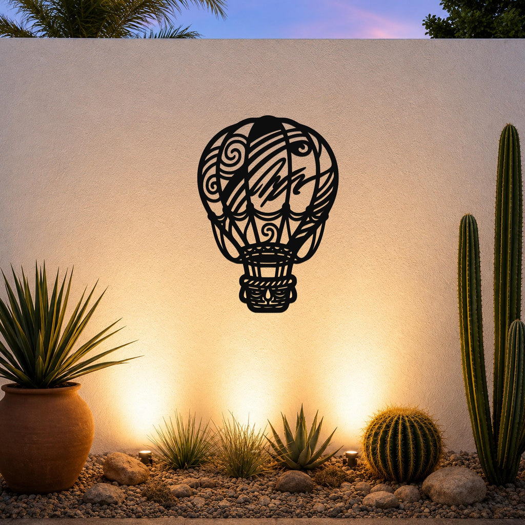 Black metal hot air balloon wall art with intricate swirl and line cutouts, mounted on an outdoor wall above a desert garden with cacti and warm uplighting.