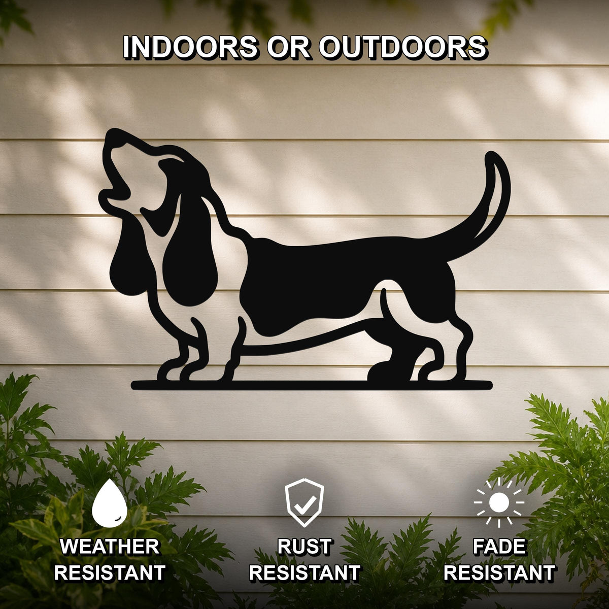 Black metal wall art silhouette of a howling basset hound, mounted on a light-colored outdoor wall with greenery below.