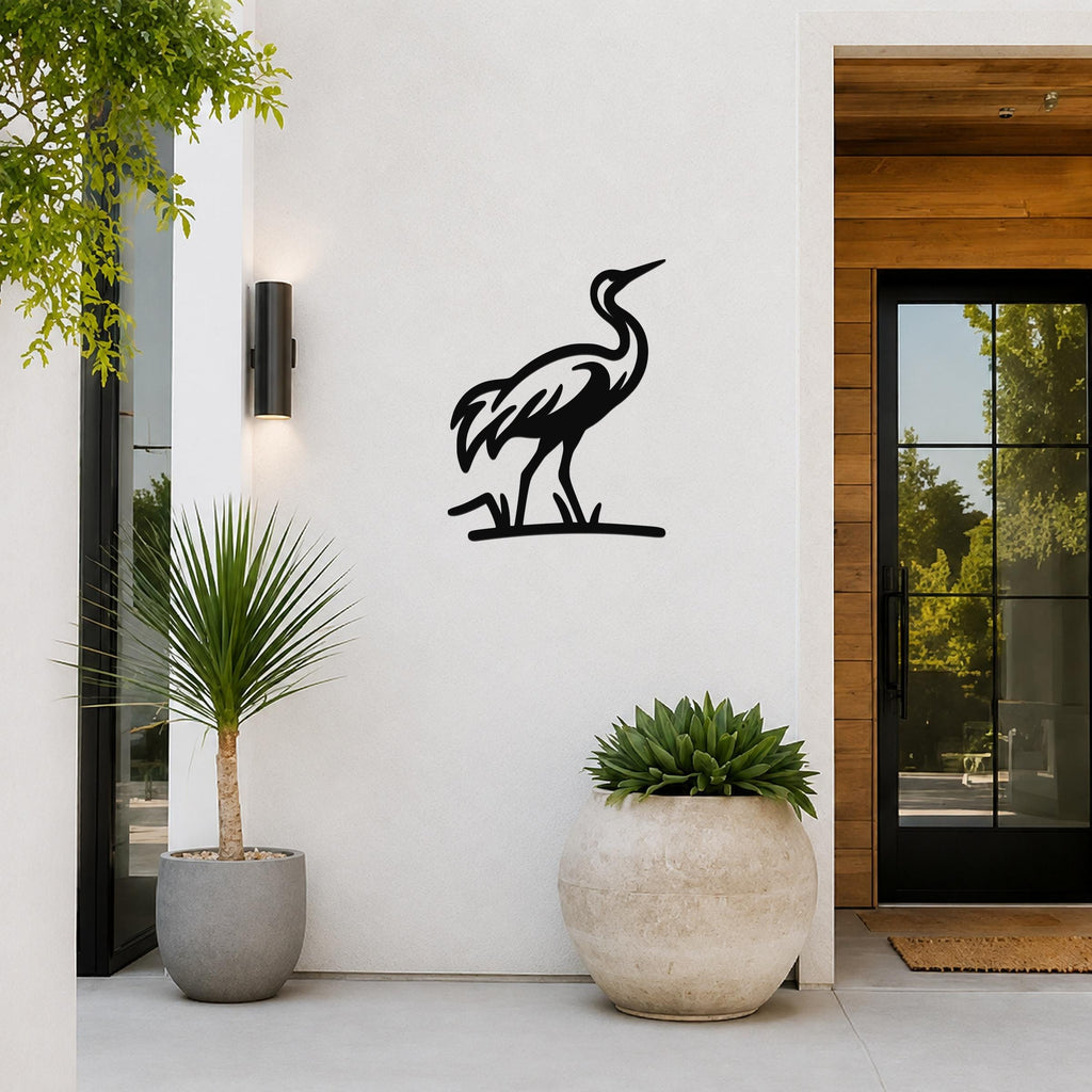 Black metal crane wall art in silhouette style, mounted on a white exterior wall beside a glass door and potted plants.