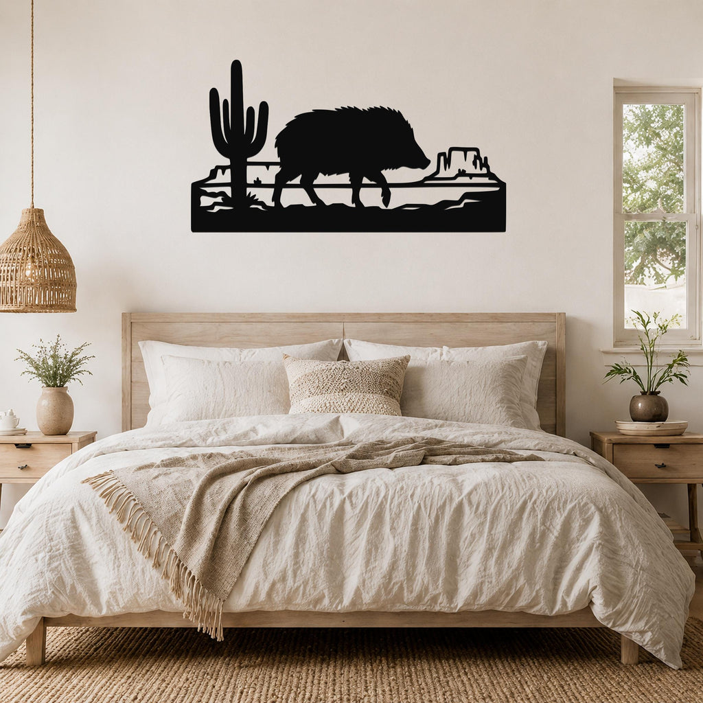 Black metal wall art silhouette of a javelina and cactus in a canyon scene, mounted above a bed in a bedroom.