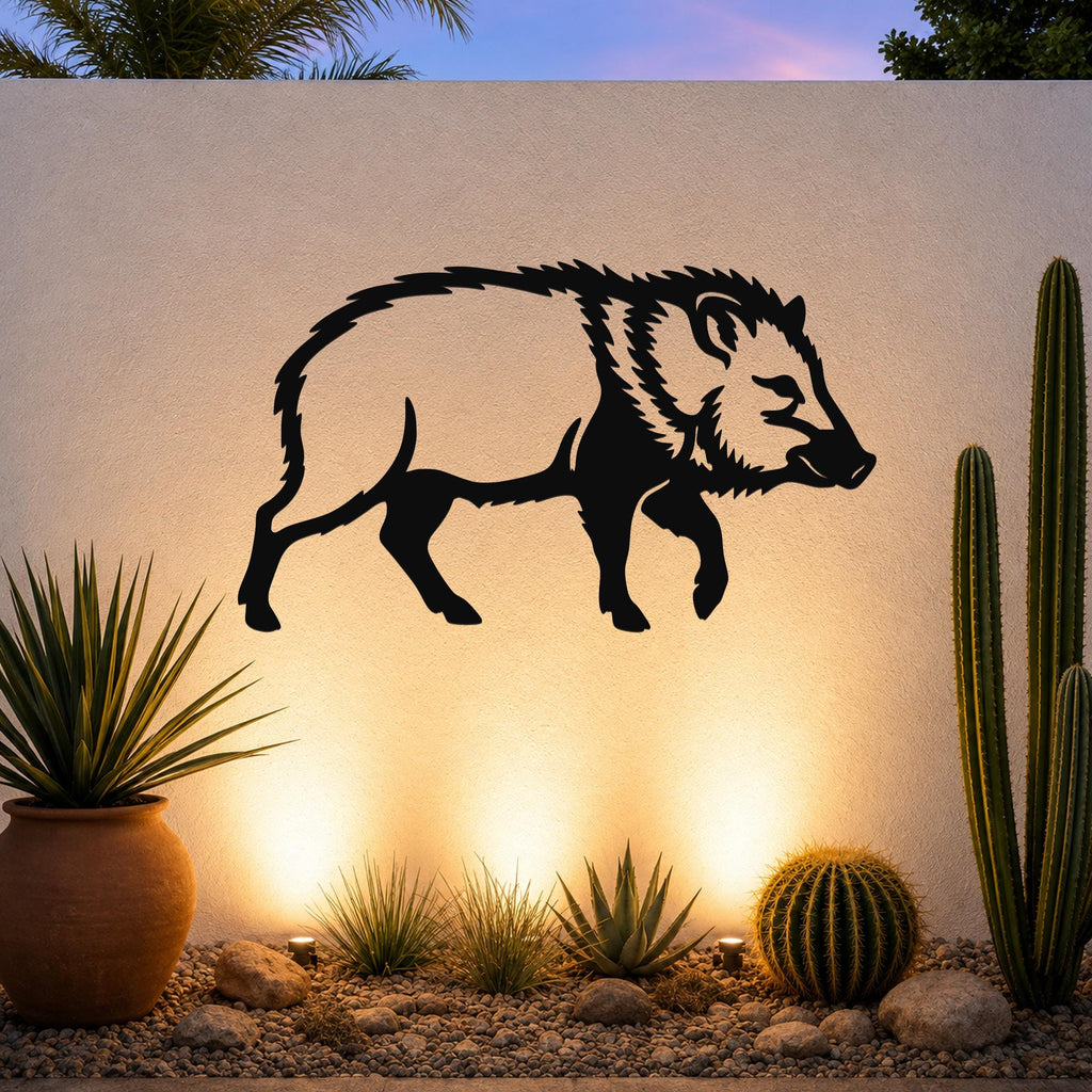 Black metal javelina wall art silhouette mounted on a textured outdoor wall above a desert garden with cacti and warm uplighting.