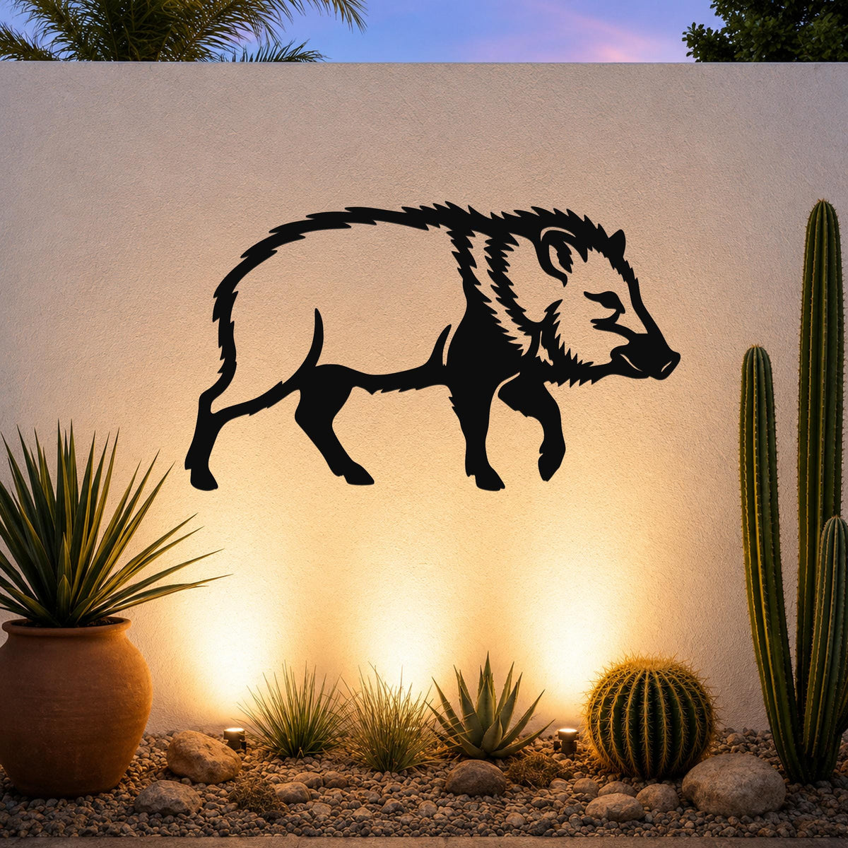 Black metal javelina wall art silhouette mounted on a textured outdoor wall above a desert garden with cacti and warm uplighting.
