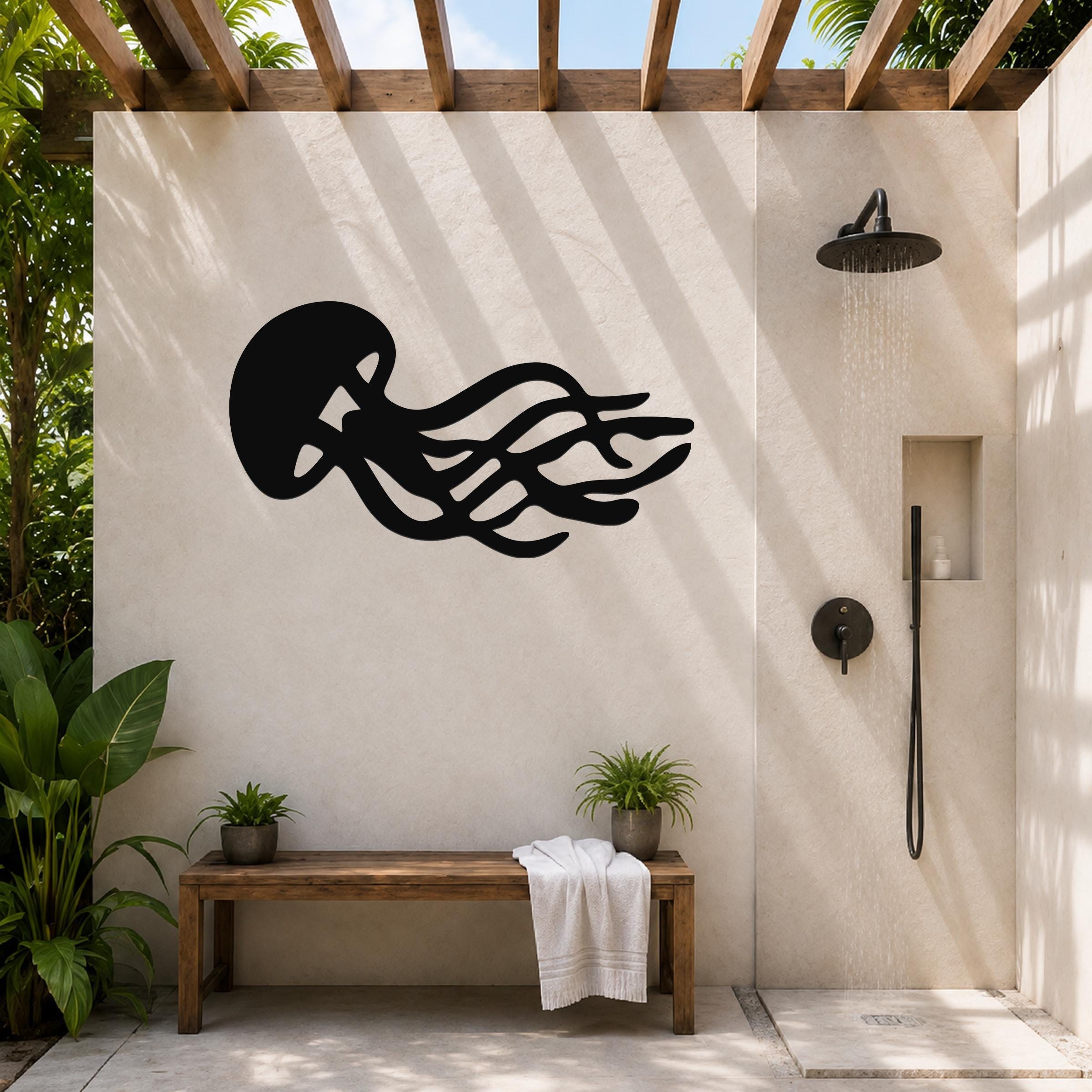 Black metal jellyfish wall art with flowing tentacle cutouts, mounted on a beige outdoor shower wall under a wooden pergola.