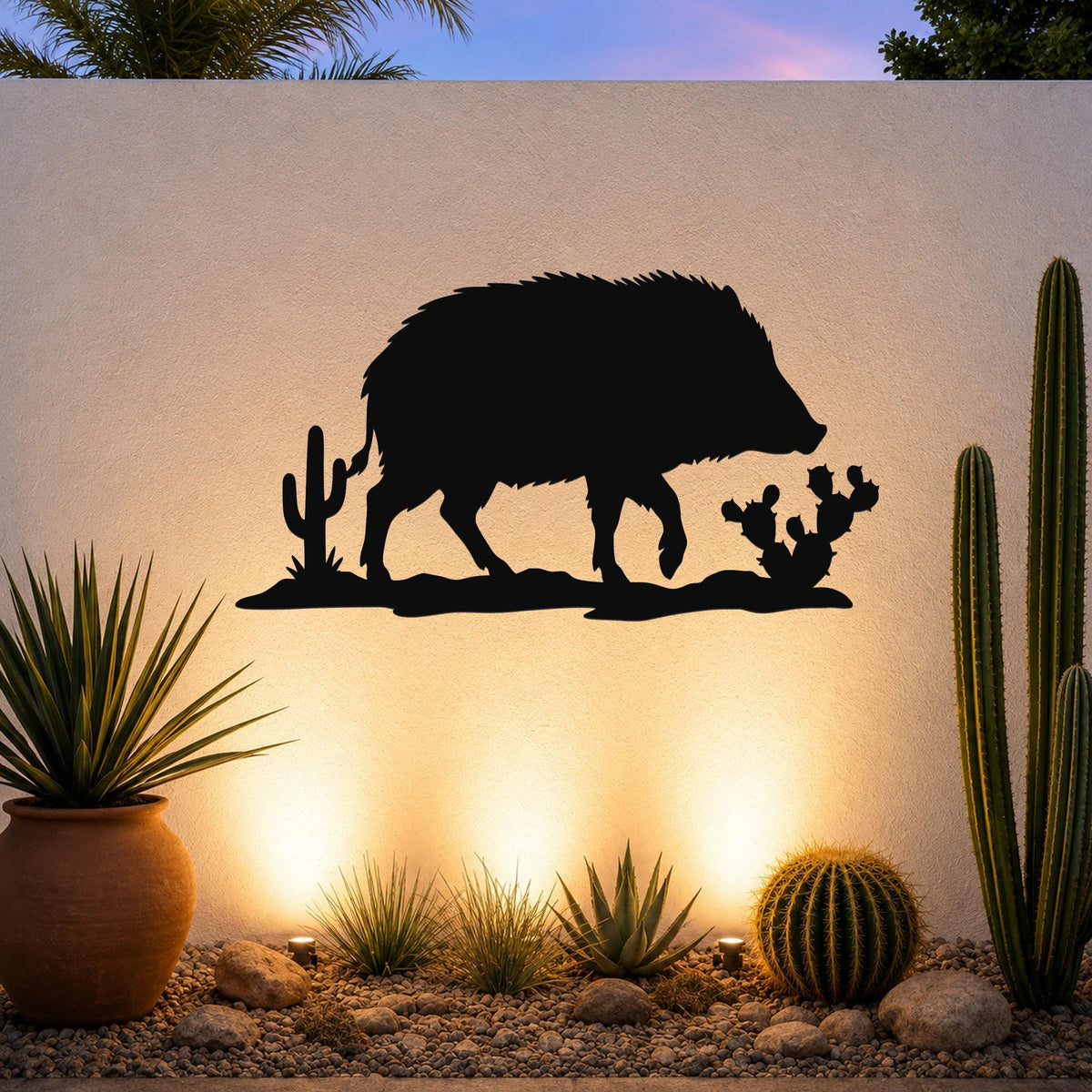 Black metal wall art silhouette of a javelina with cacti, mounted on an outdoor wall above a desert garden with potted plants and ground lights.