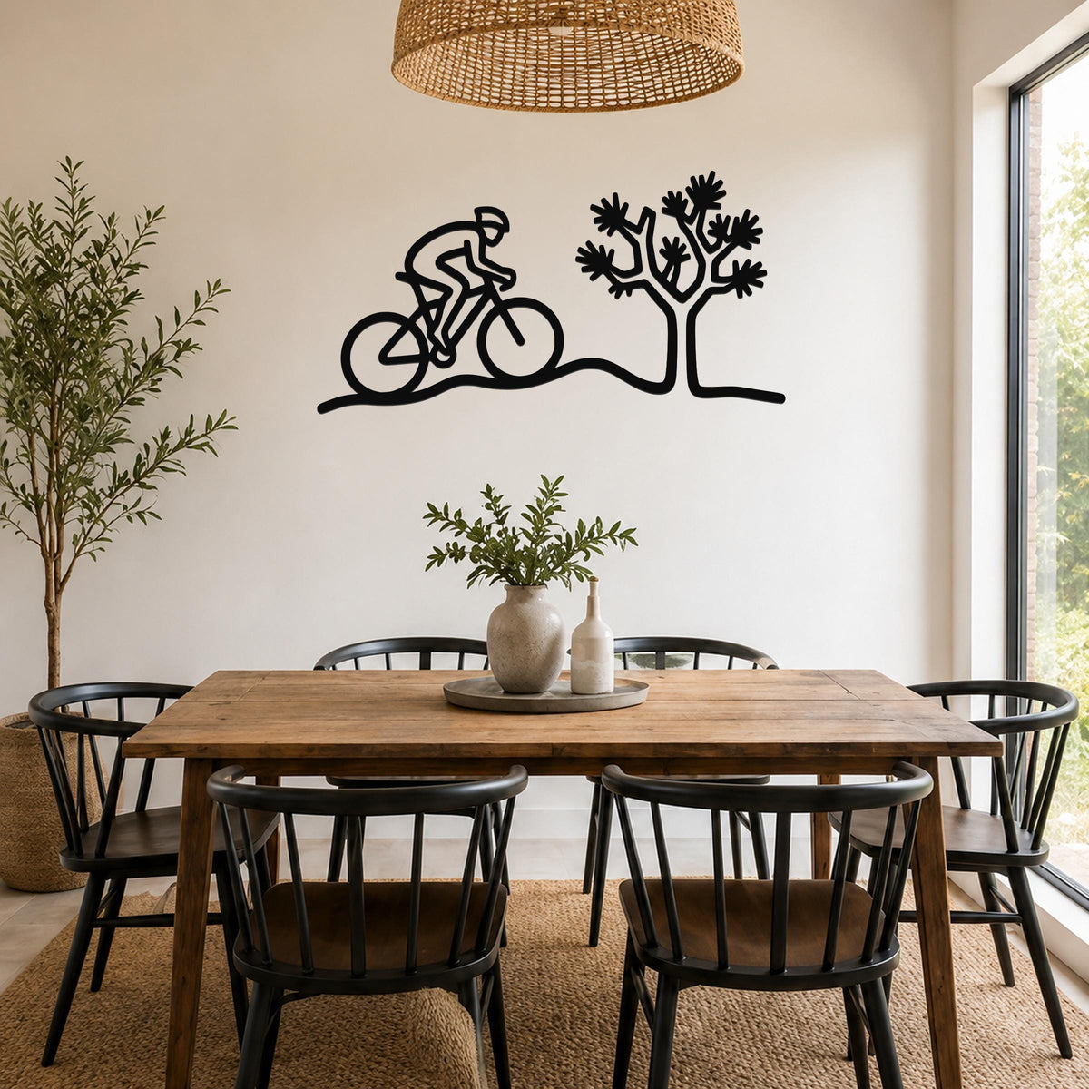 Black metal wall art silhouette of a cyclist and a Joshua tree, mounted on a dining room wall above a wooden table.