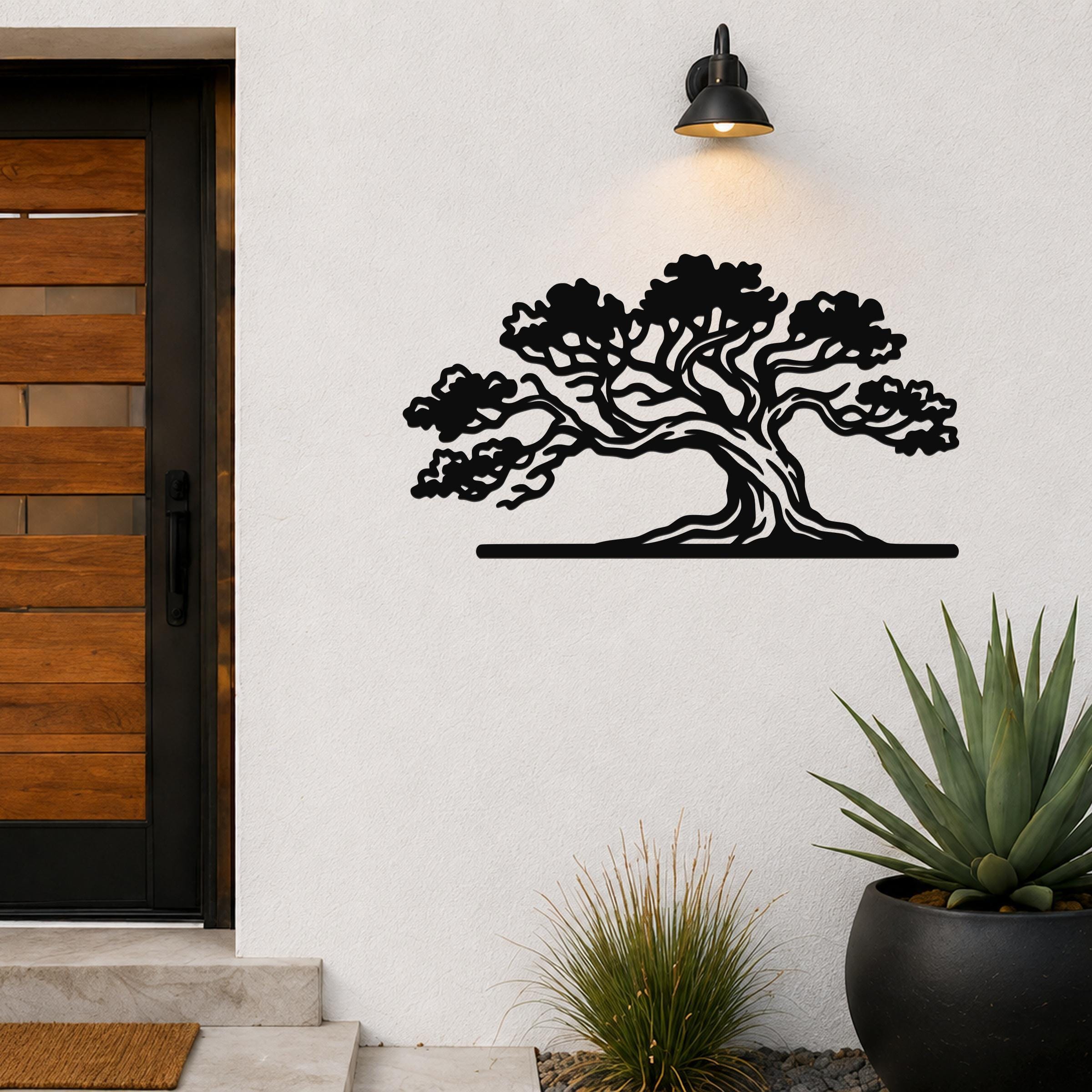 Black metal wall art silhouette of a juniper tree with detailed branches and roots, mounted on an outdoor wall beside a wooden door and potted plants.