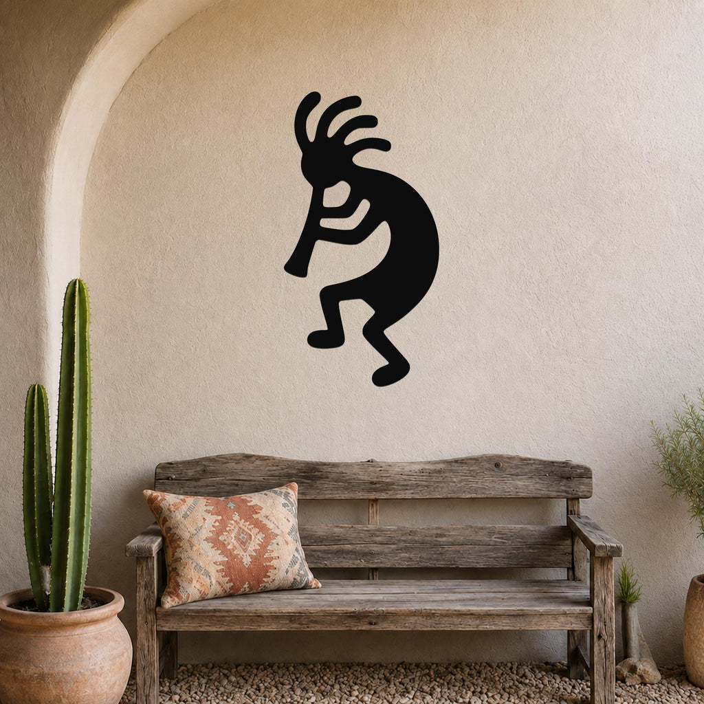 Black metal Kokopelli wall art silhouette with internal cutouts, mounted on a stucco wall above a wooden bench in a patio setting.
