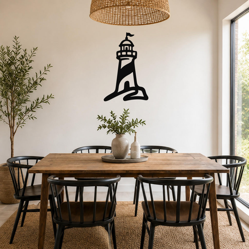Black metal lighthouse wall art with a silhouette design, mounted on a white wall above a wooden dining table in a bright room.