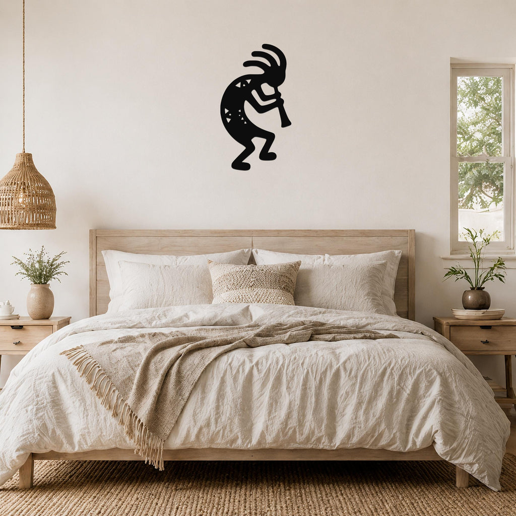 Black metal Kokopelli wall art silhouette with internal geometric cutouts, mounted on a wall above a bed in a neutral bedroom.