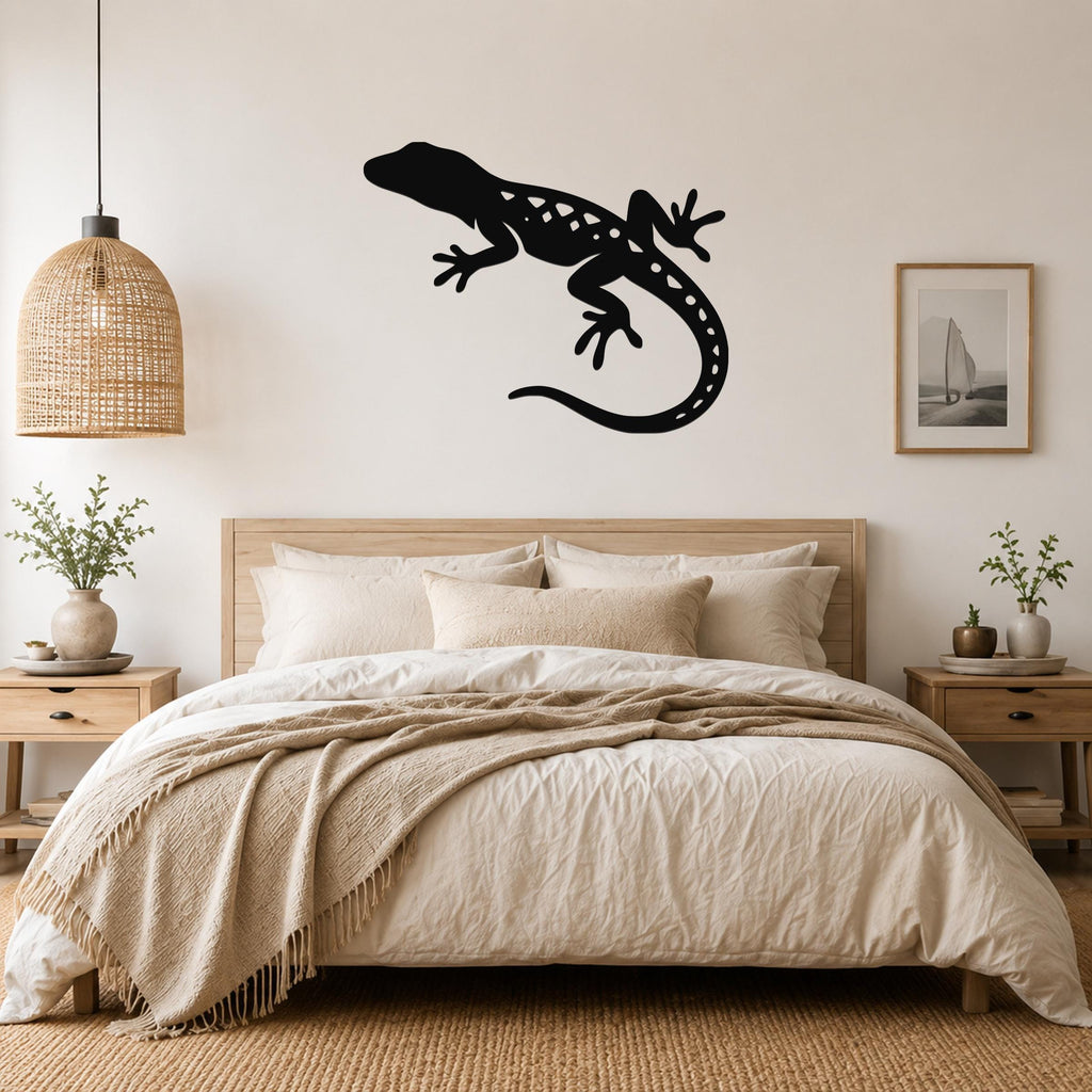 Black metal lizard wall art with internal cutout details, mounted above a bed in a neutral bedroom.