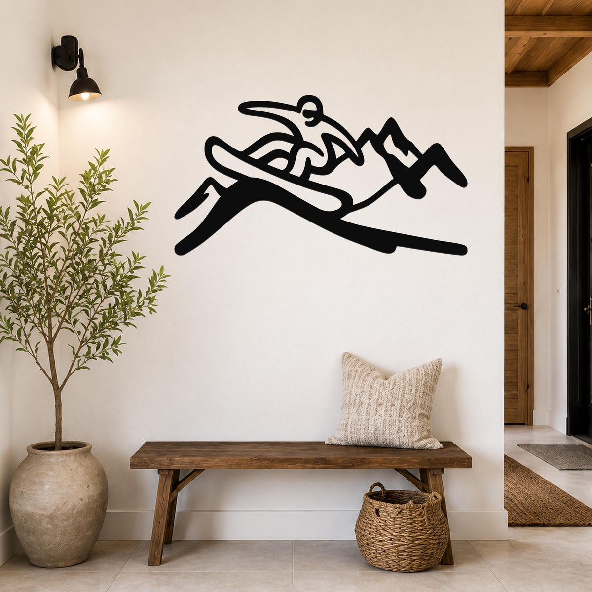 Black metal wall art silhouette of a snowboarder in motion, mounted above a wooden bench in a hallway.