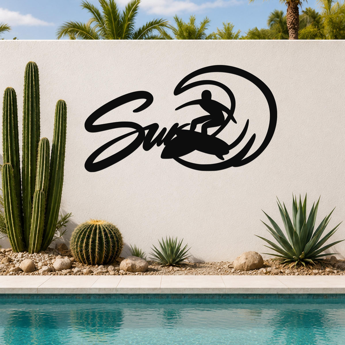 Black metal surfer silhouette wall art with wave cutout, mounted on a white outdoor wall beside a pool and cacti.