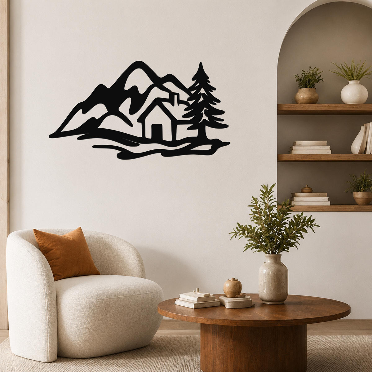 Black metal wall art silhouette of a mountain cabin scene with trees and peaks, mounted on a living room wall above a white armchair.