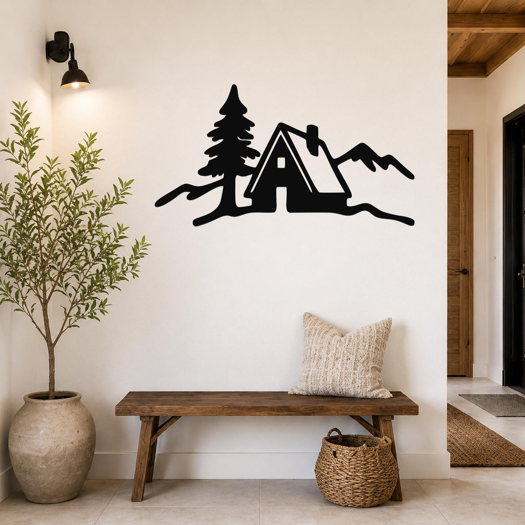 Black metal wall art silhouette of a cabin, pine tree, and mountains, mounted on a white wall above a wooden bench in a hallway.