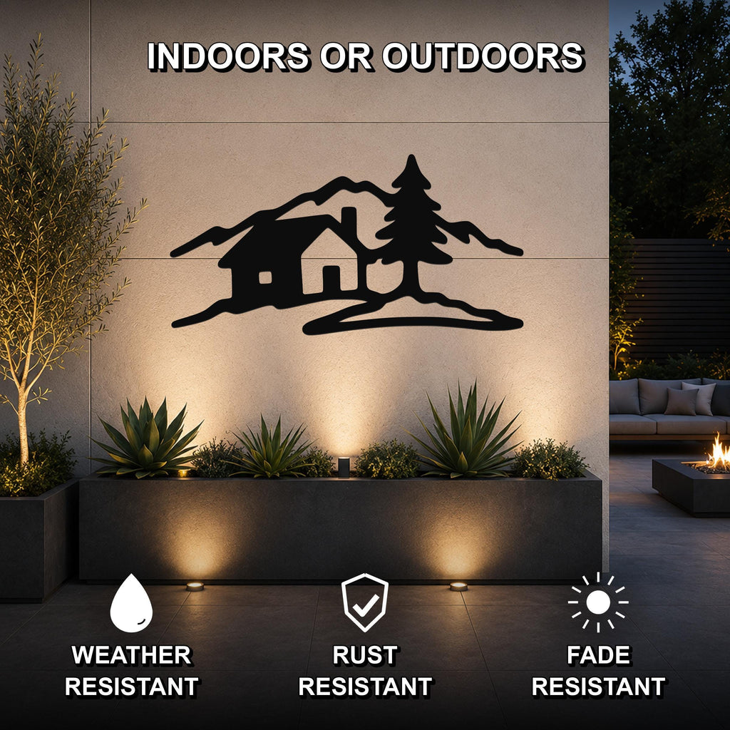 Black metal wall art with a silhouette of a cabin, pine tree, and mountains, mounted on an outdoor wall above a planter in a patio setting.