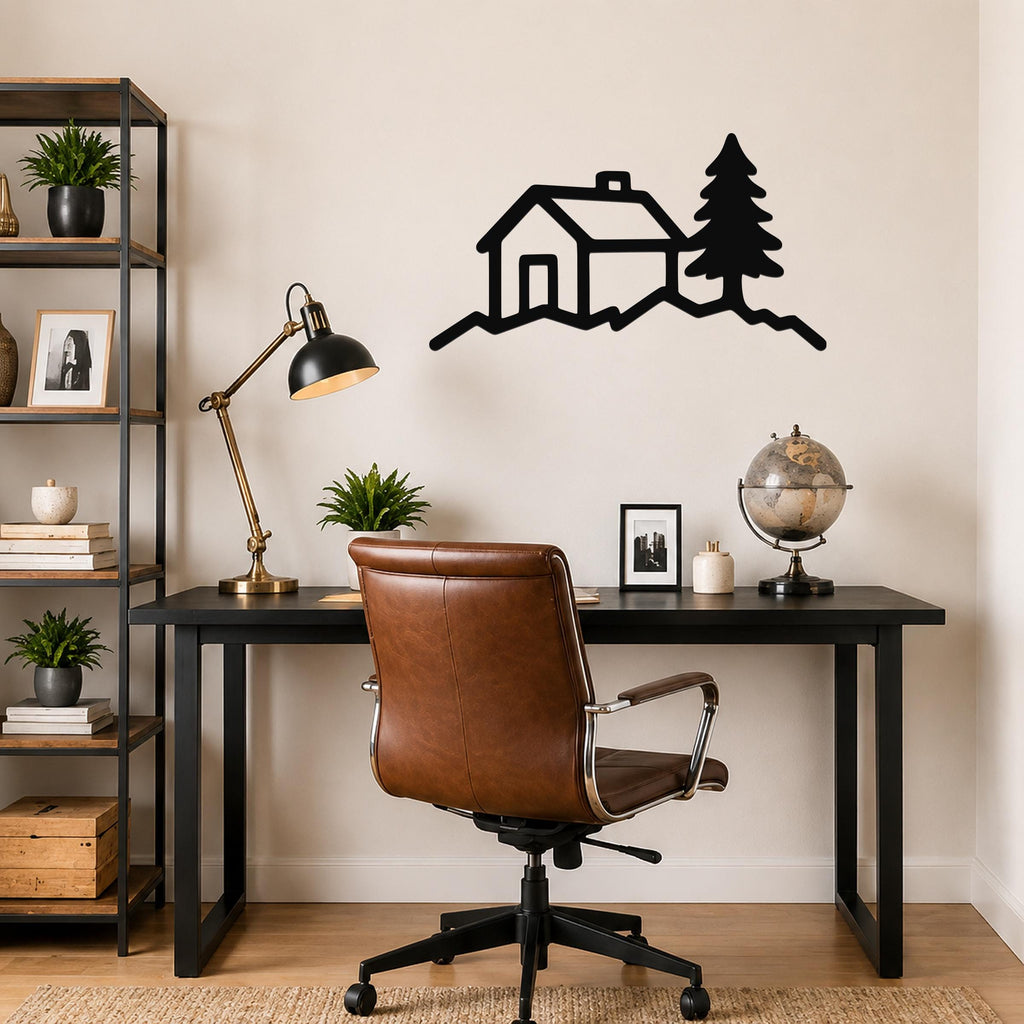 Black metal wall art silhouette of a cabin and pine tree on a hill, mounted above a black desk in a home office.