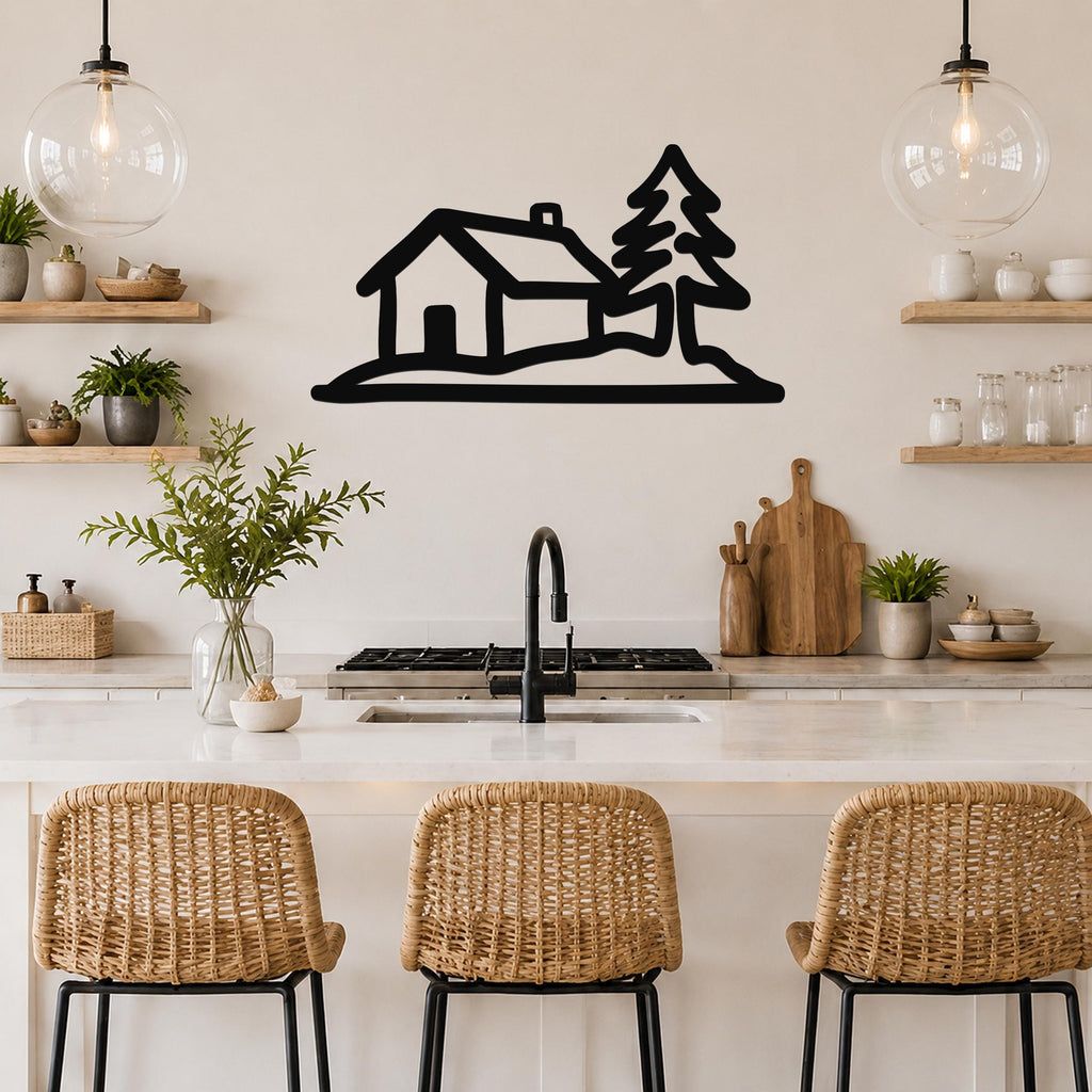 Black metal wall art silhouette of a cabin and pine tree, mounted above a kitchen counter with wicker stools and open shelving.
