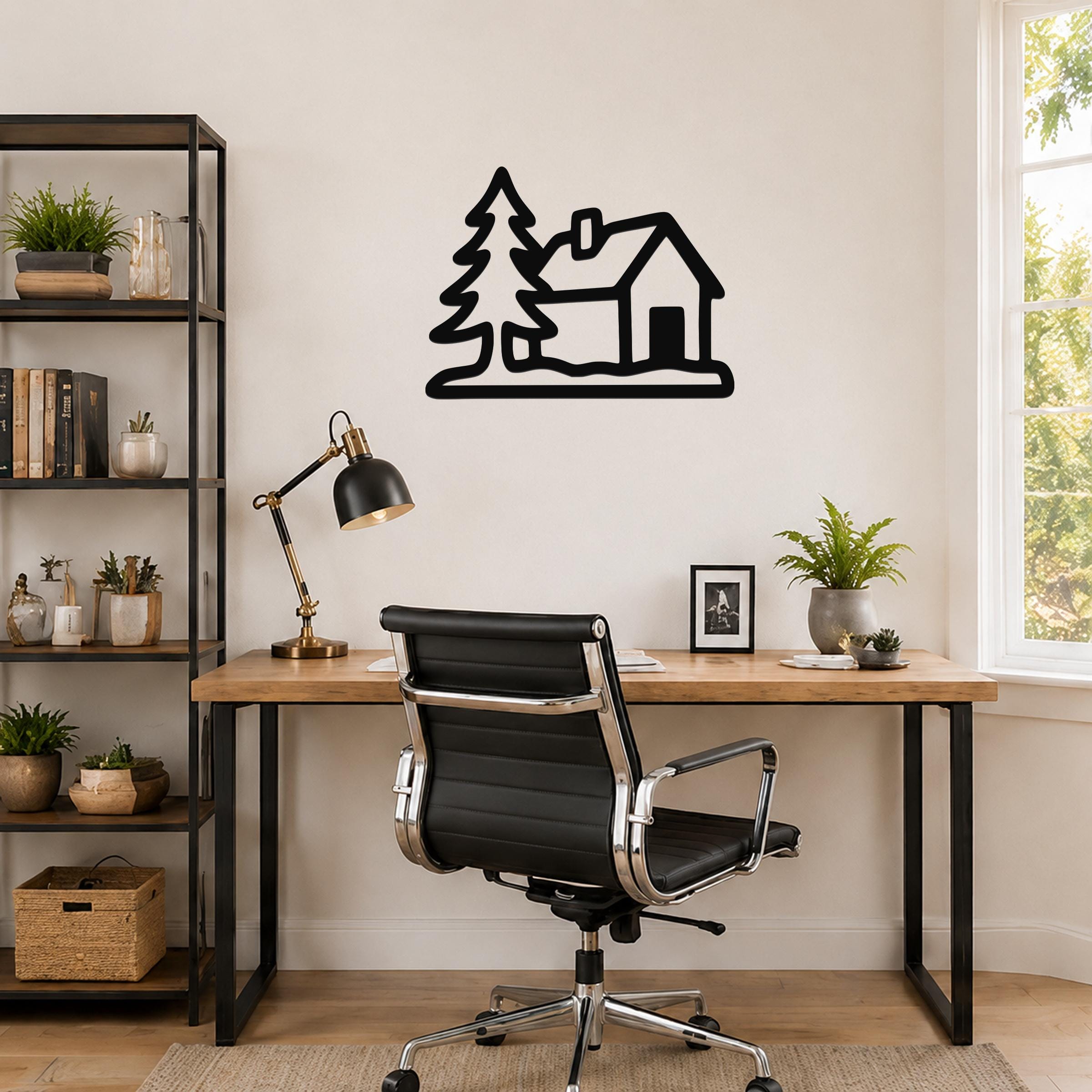 Black metal wall art silhouette of a cabin and pine tree, mounted on a wall above a wooden desk in a home office.