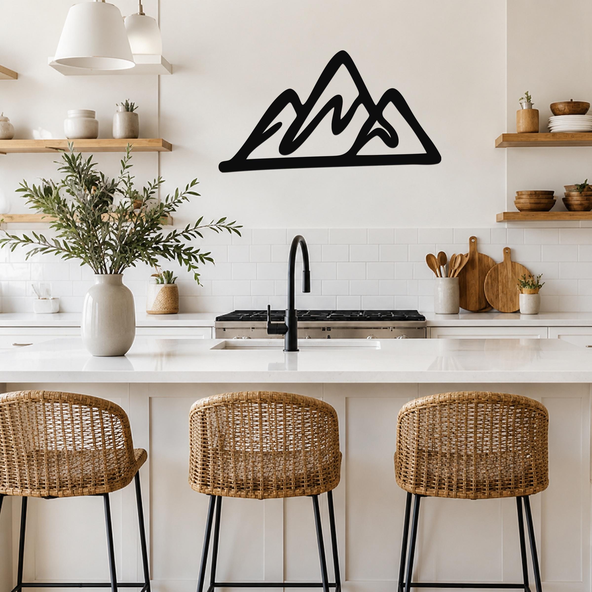 Black metal mountain silhouette wall art with layered peaks, mounted on a kitchen wall above a white countertop.