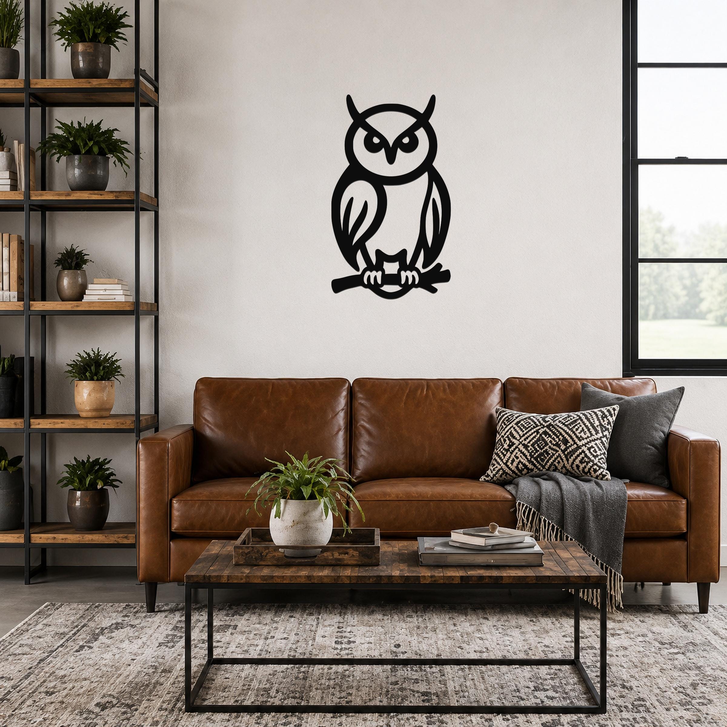Black metal owl wall art with cutout details, mounted on a living room wall above a brown leather sofa.