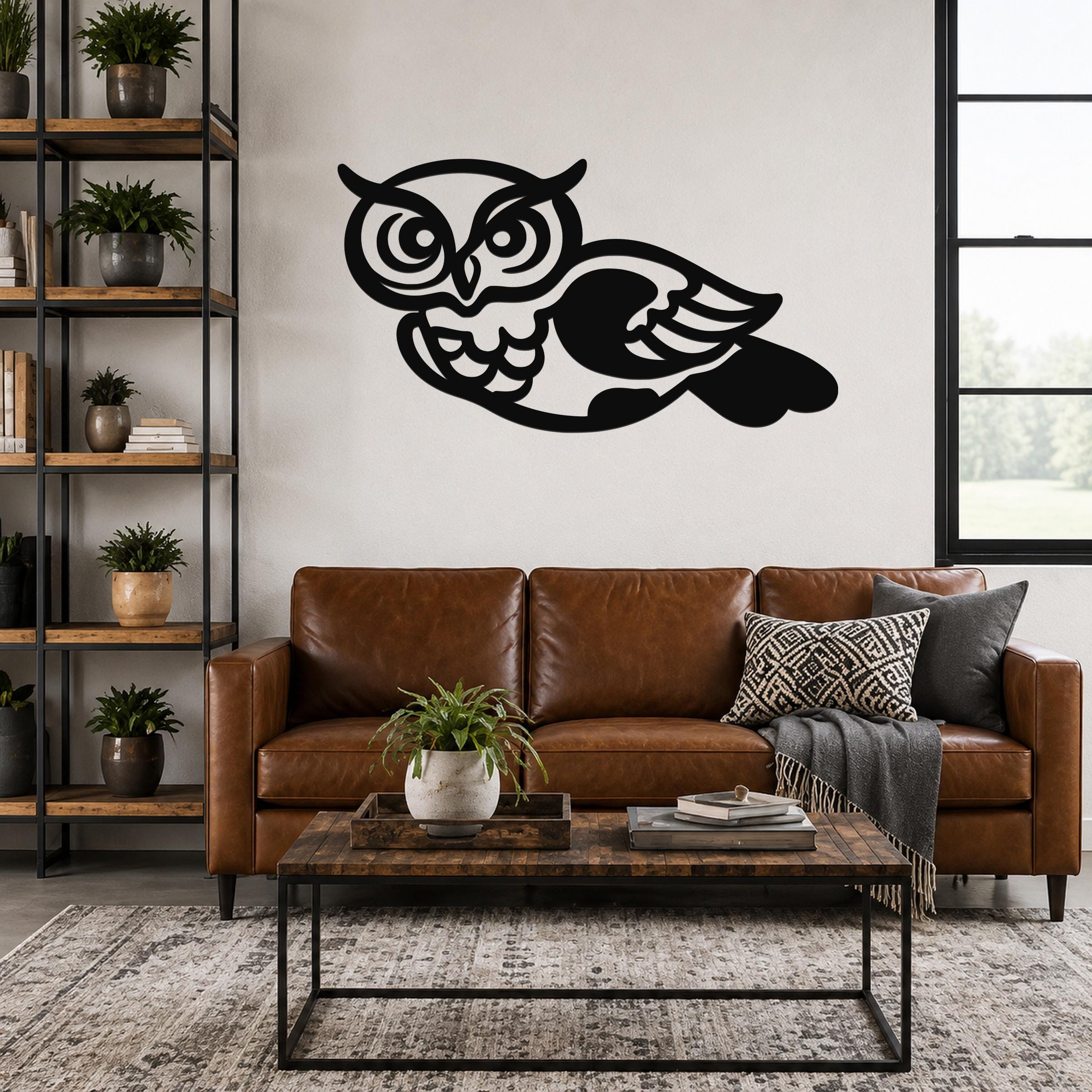Black metal owl wall art with cutout eyes and wings, mounted above a brown leather sofa in a living room.