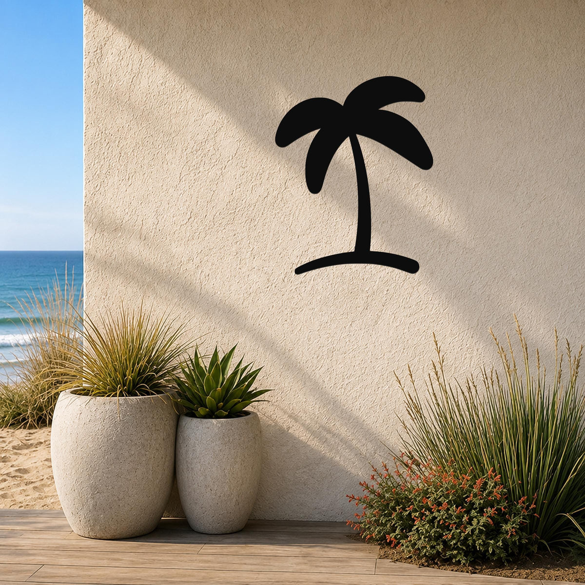 Black metal palm tree wall art silhouette mounted on a textured beige outdoor wall, above potted plants on a wooden deck near the ocean.